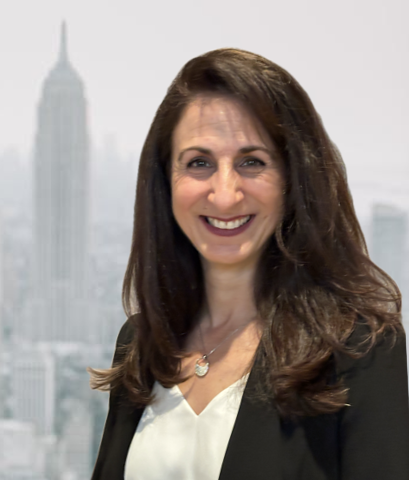 Woman with long brown hair smiling in front of a city skyline with a tall building in the background.