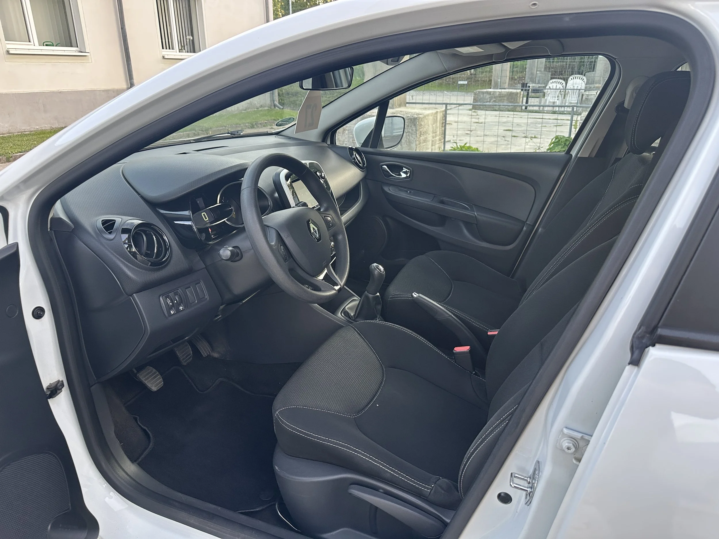 Innenraum eines weißen Autos, Ansicht von der Fahrerseite, zeigt Lenkrad, Armaturenbrett und vorderer Sitz.