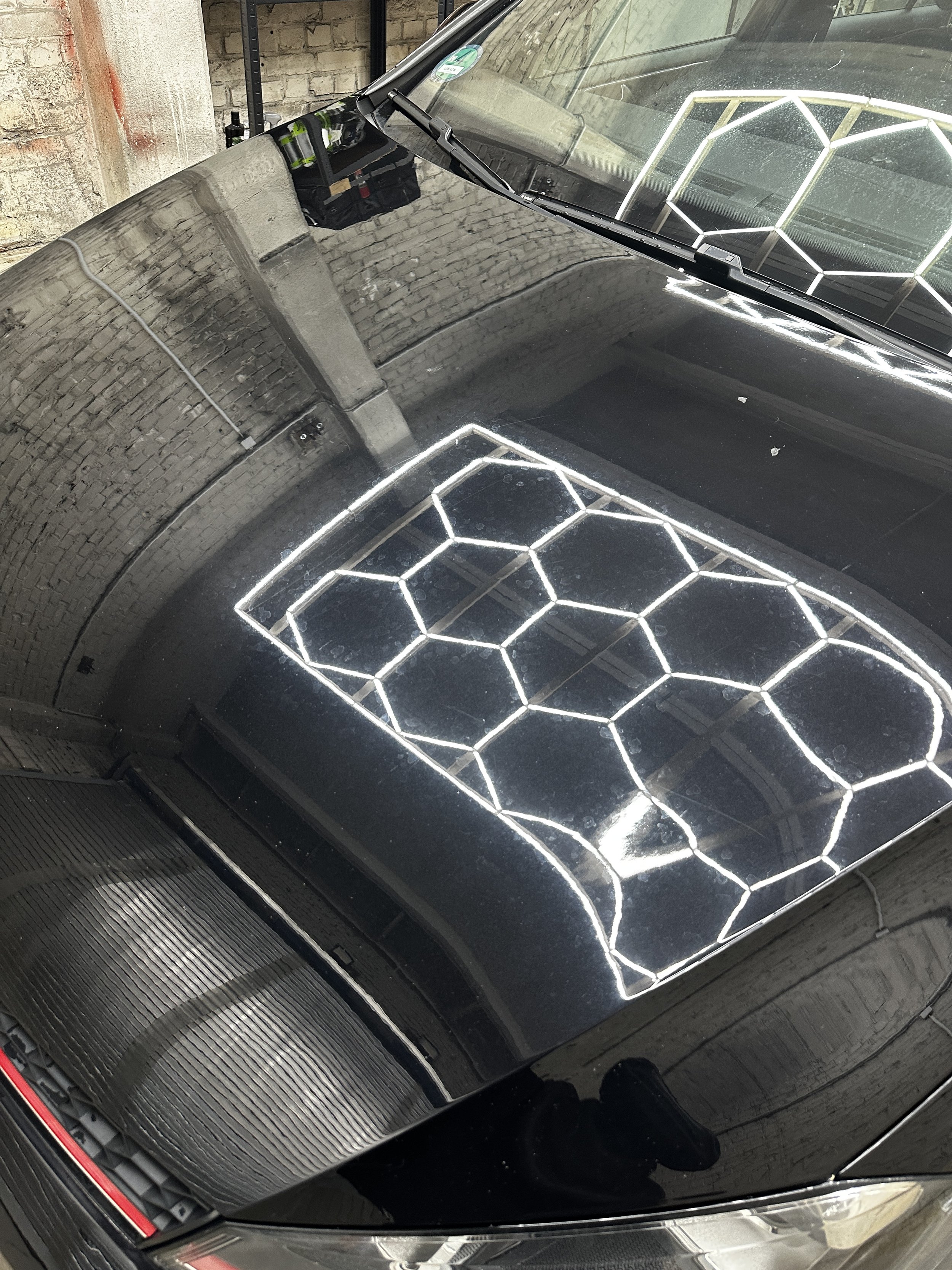 Nahaufnahme eines schwarzen Autos mit reflektierendem Lack und ein geometrisches neon-weißes Lichtdesign auf der Motorhaube, das die Form eines Hexagons bildet.