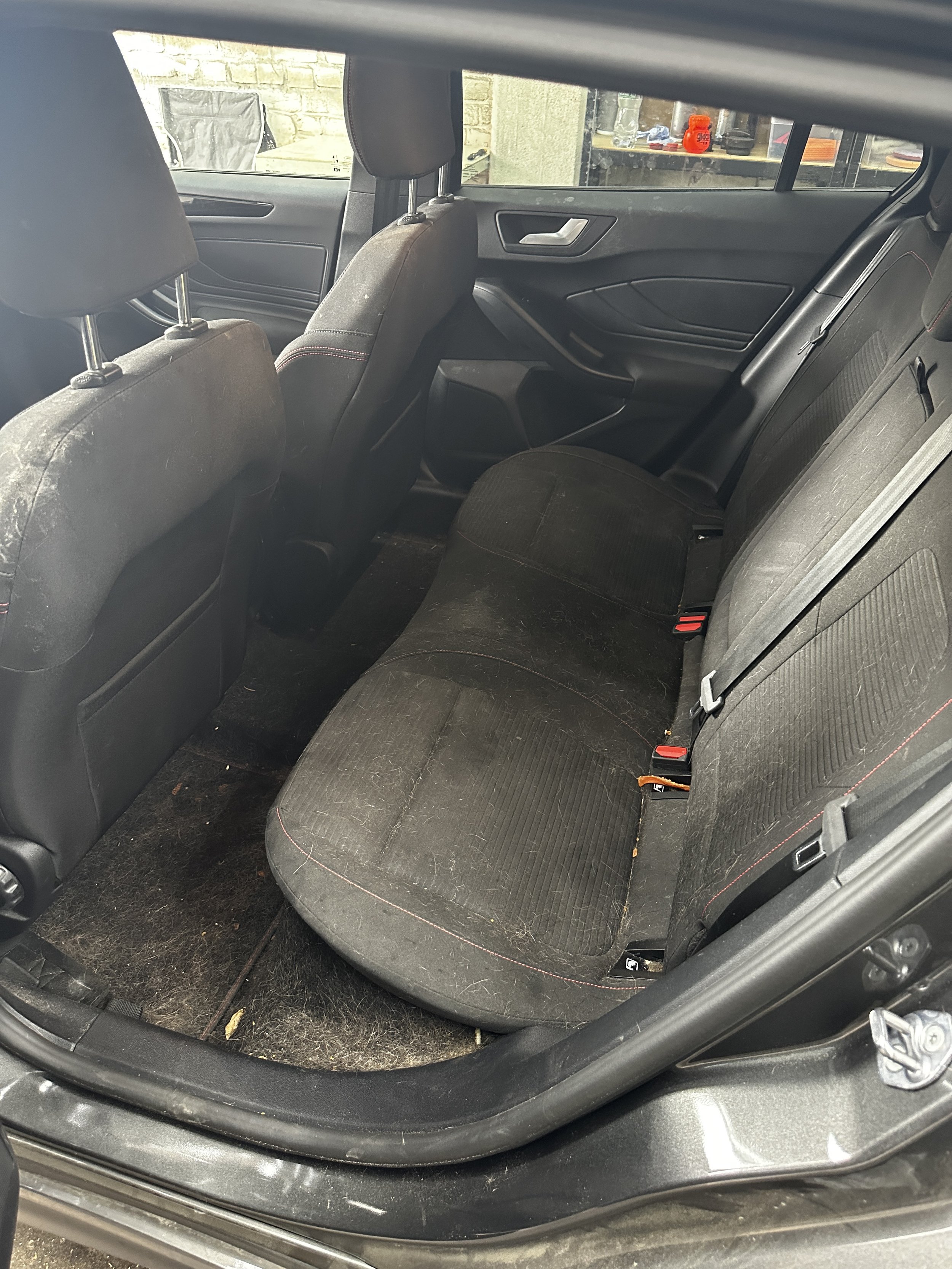 Der Blick in den Kofferraum eines Autos zeigt die hintere Sitzbank, die innen schmutzig und mit Staub sowie kleinen Partikeln bedeckt ist.