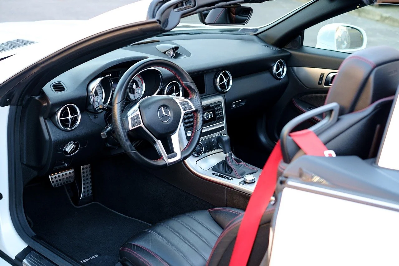 Innenraum eines Mercedes-Benz Sportwagens mit schwarzer Lederexklusivausstattung, Lenkrad mit Mercedes-Stern, manuelle Schalthebel, Sportsitze, runde Lüftungsöffnungen und Automatiksteuerung.