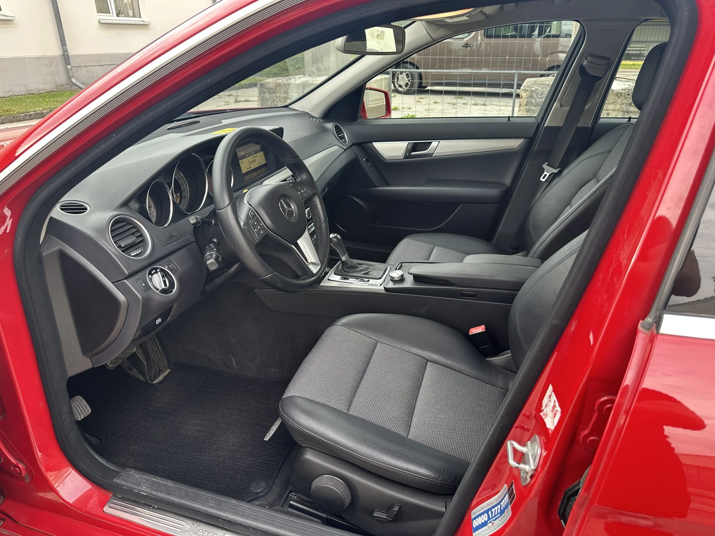 Innenraum eines roten Mercedes-Benz Fahrzeugs, sichtbare Instrumententafel, Lenkrad und vorderer Sitz.