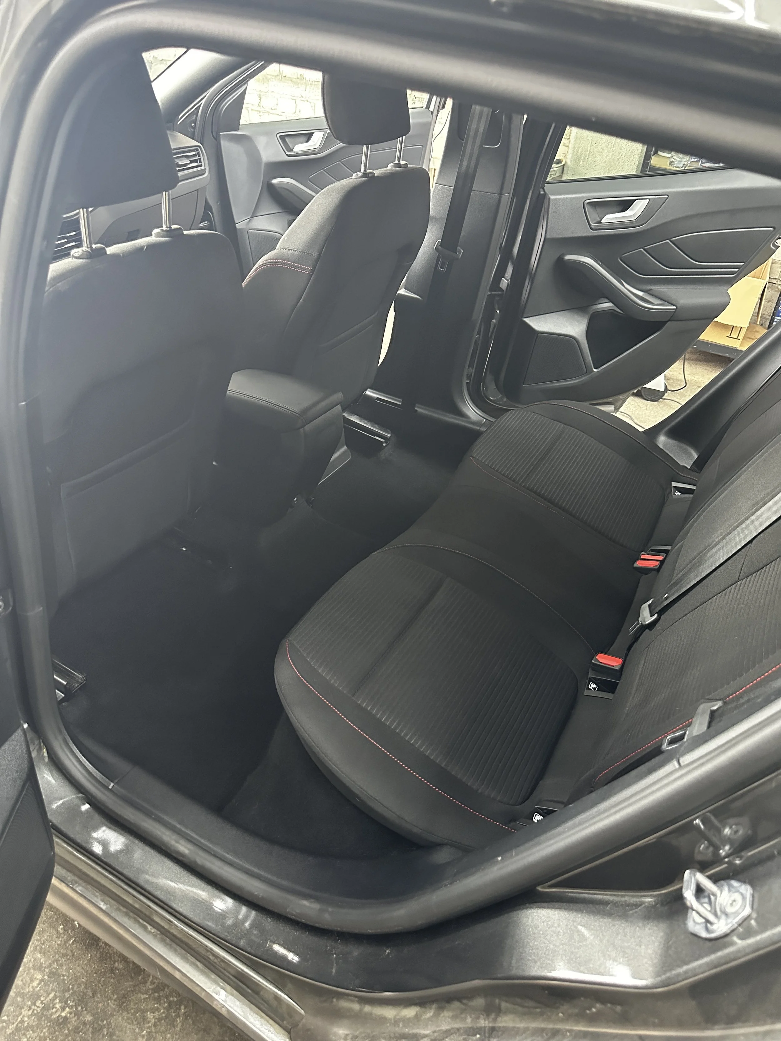 Innenraum eines Autos, Blick auf die Rücksitze und die vorderen Sitze, die Tür auf der Fahrerseite ist offen, im Hintergrund sind Lagerregale mit Kartons.