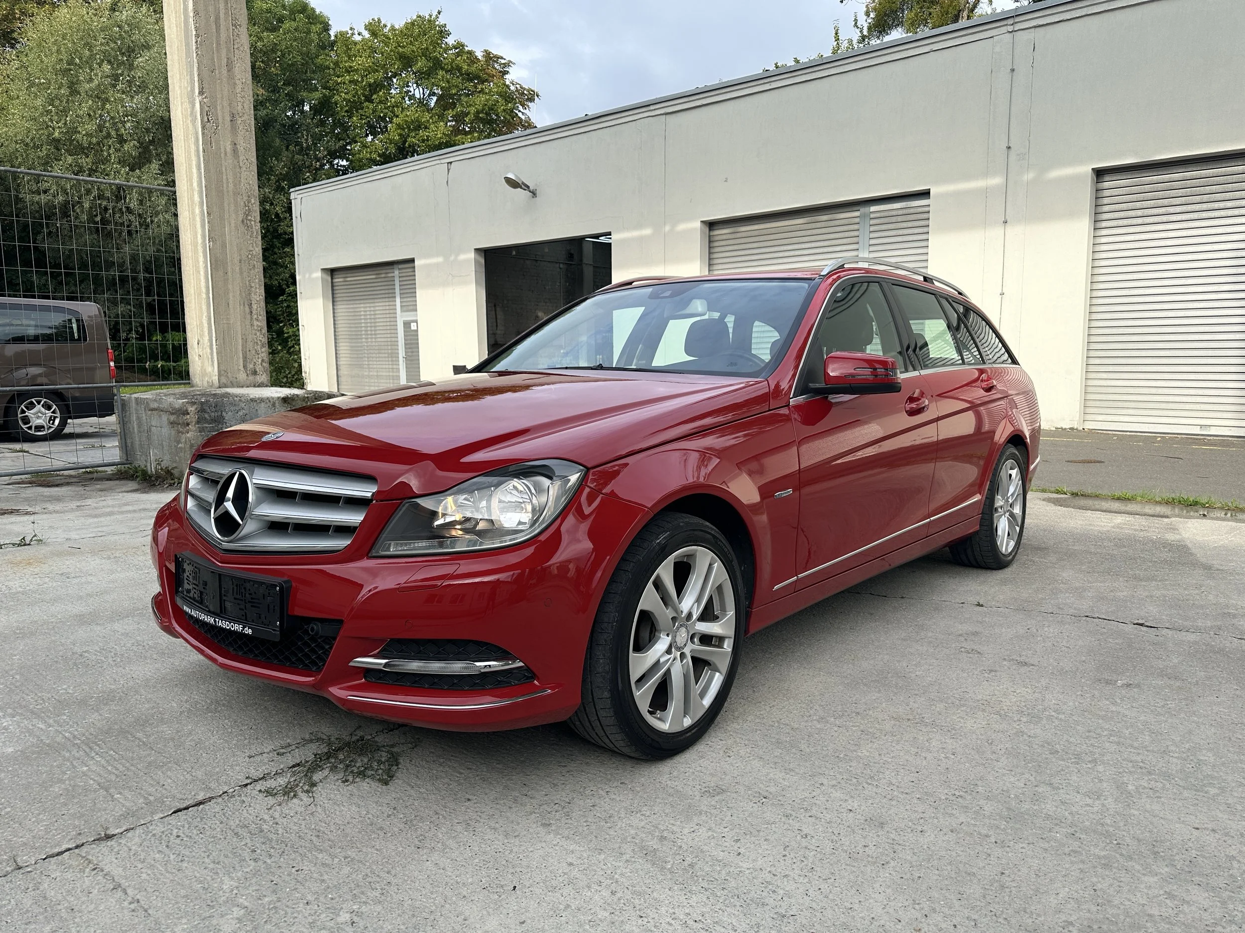 Ein rotes Mercedes-Benz Auto parkt vor einer weißen Industriehalle mit horizontalen Rolltoren.