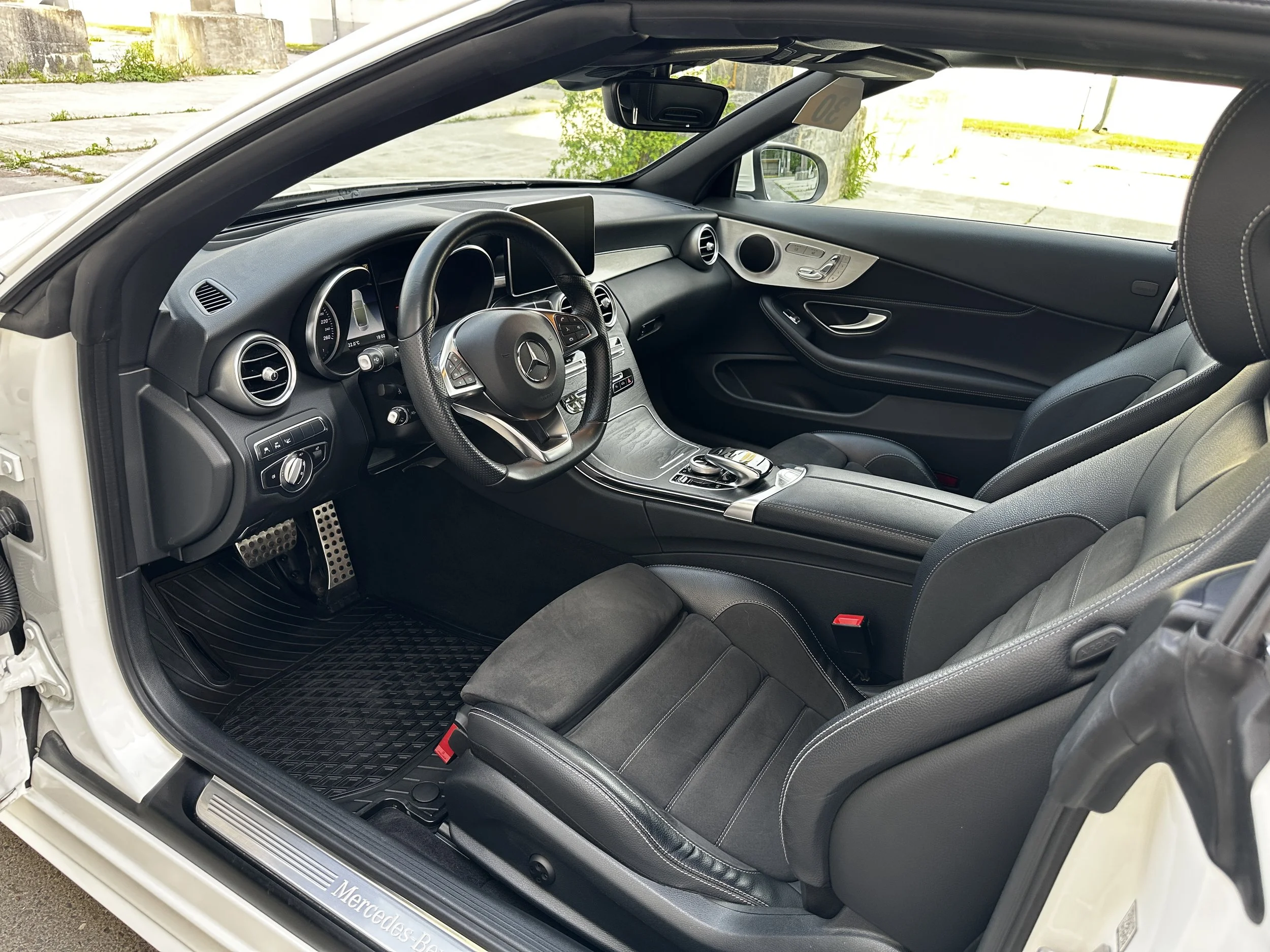 Innenansicht eines modernen Mercedes-Benz Autos mit schwarzem Armaturenbrett, Multifunktionslenkrad, Touchscreen-Display und Ledersitzen, Blick auf die Fahrerseite.