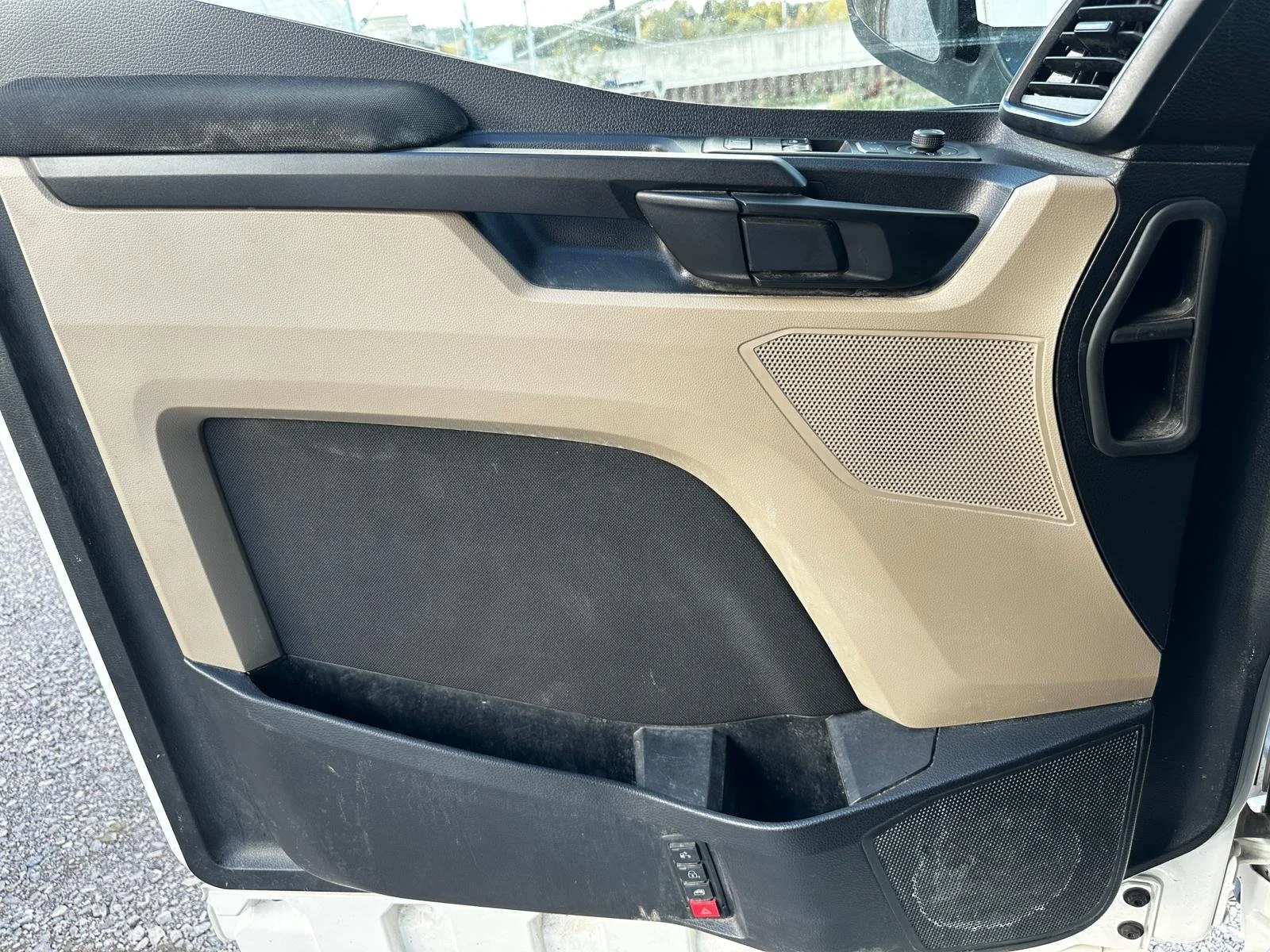 Innenansicht einer Fahrertür eines Fahrzeugs mit schwarzem und beigem Kunststoffinterieur, Lautsprechern, Türgriffen und Bedienelementen.