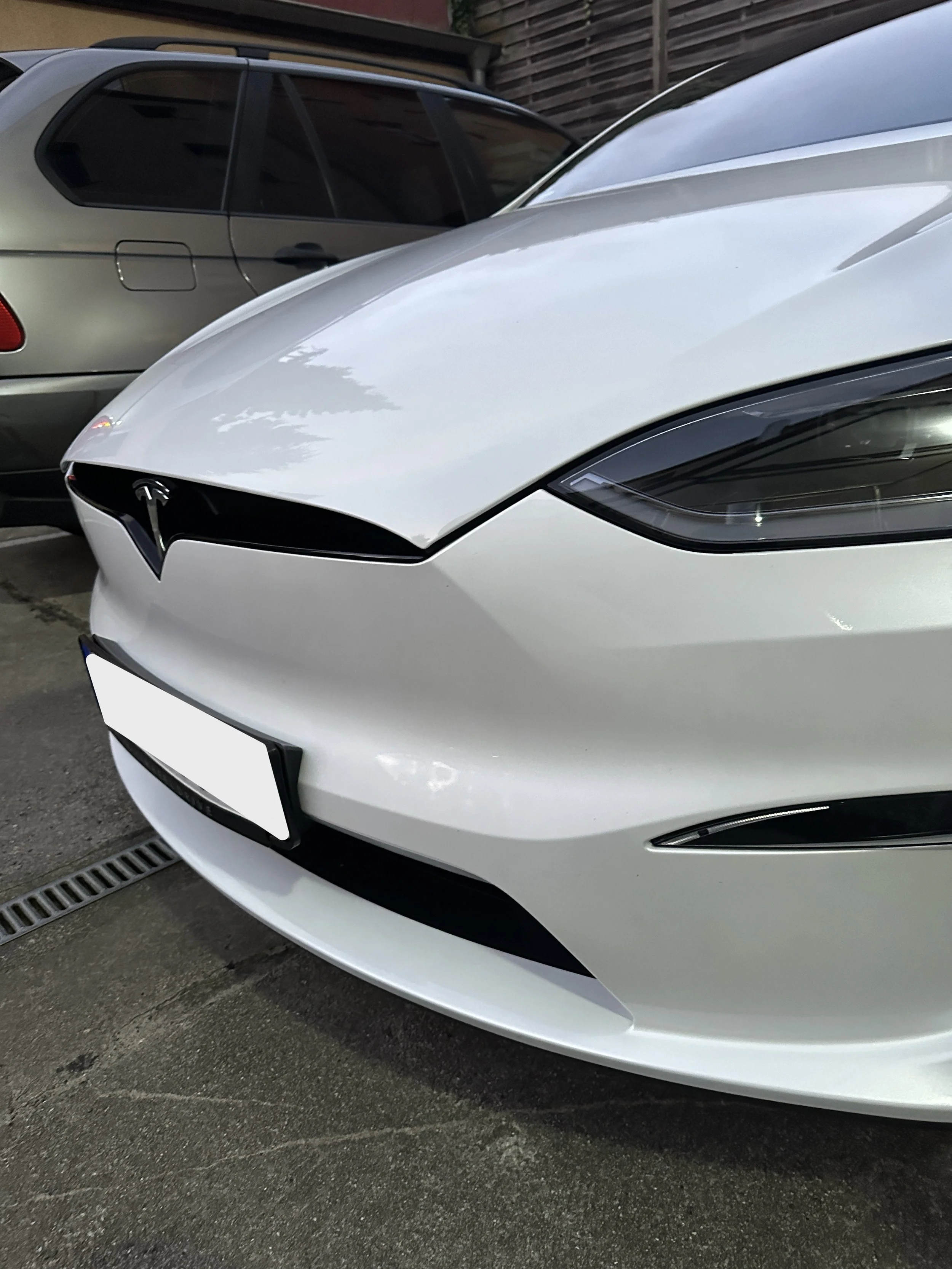 Weiße Tesla-Fahrzeug vor einem grauen Auto, geparkt auf einer Straße mit einem Ablaufschacht im Vordergrund