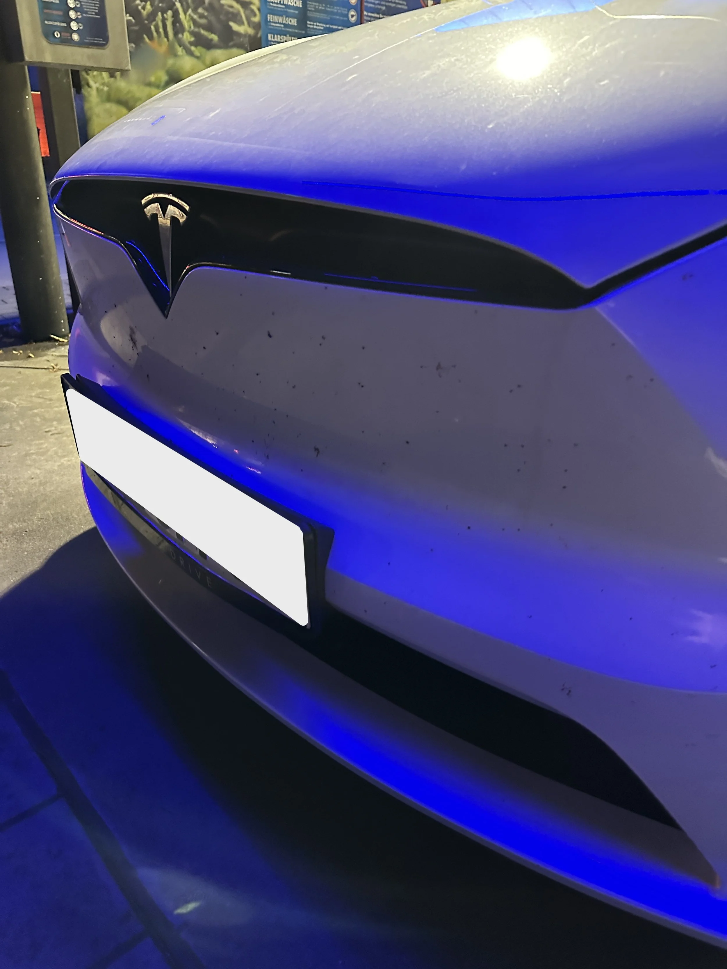 Vorderseite eines weißen Tesla-Autos mit sichtbarem Logo, parkend bei Nacht in dunkler Umgebung.