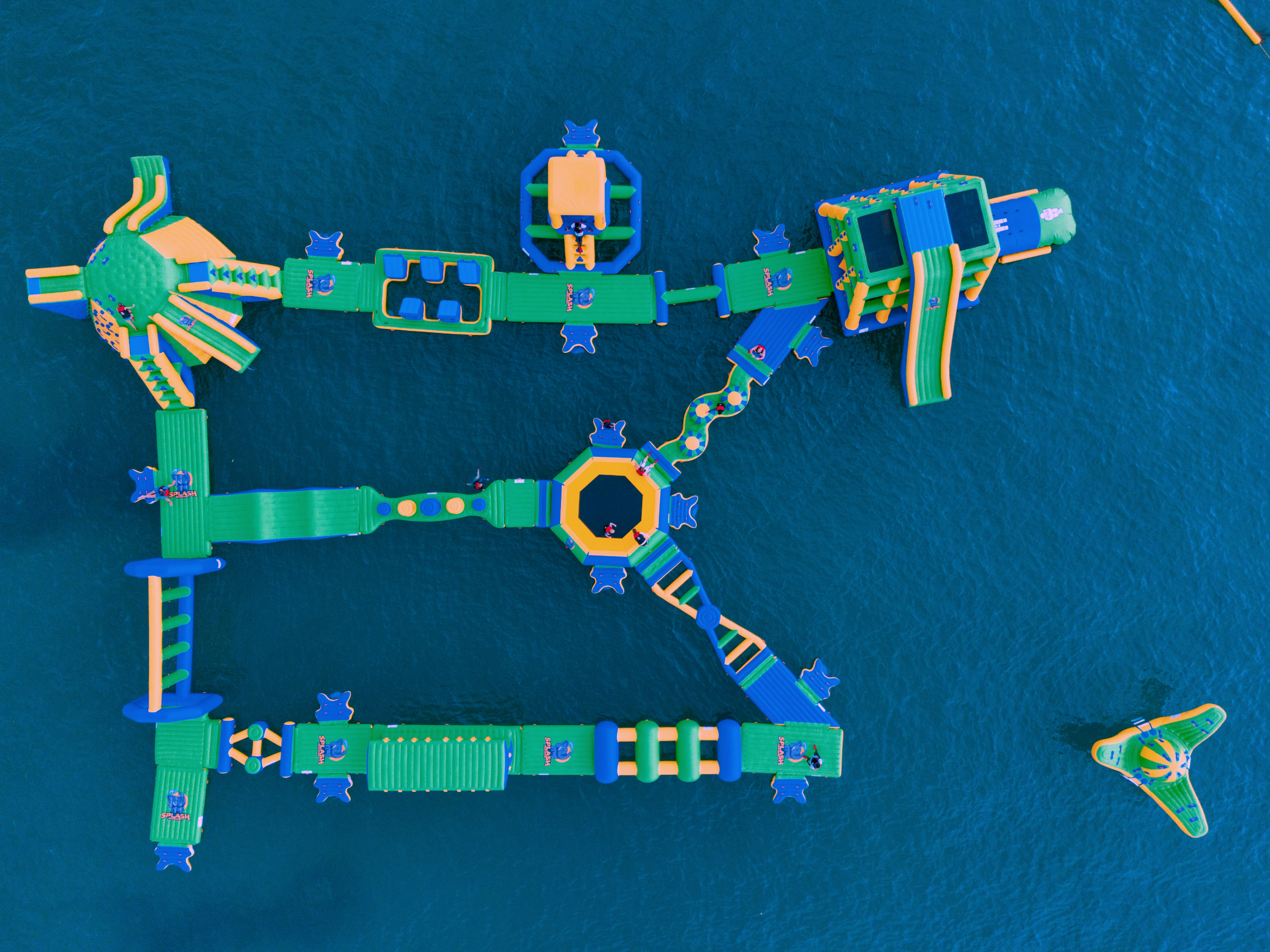 Colorful inflatable water park with multiple slides, climbing structures, and a trampoline, situated on a large body of water.
