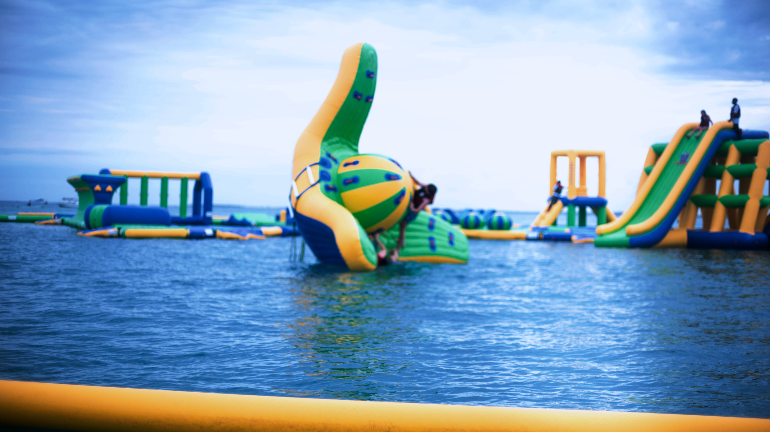 Colorful inflatable water obstacle course on the ocean with slides and climbing structures, and people playing on it.