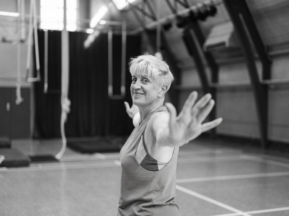 A senior woman in athletic clothing stretching her arms in a gymnasium.