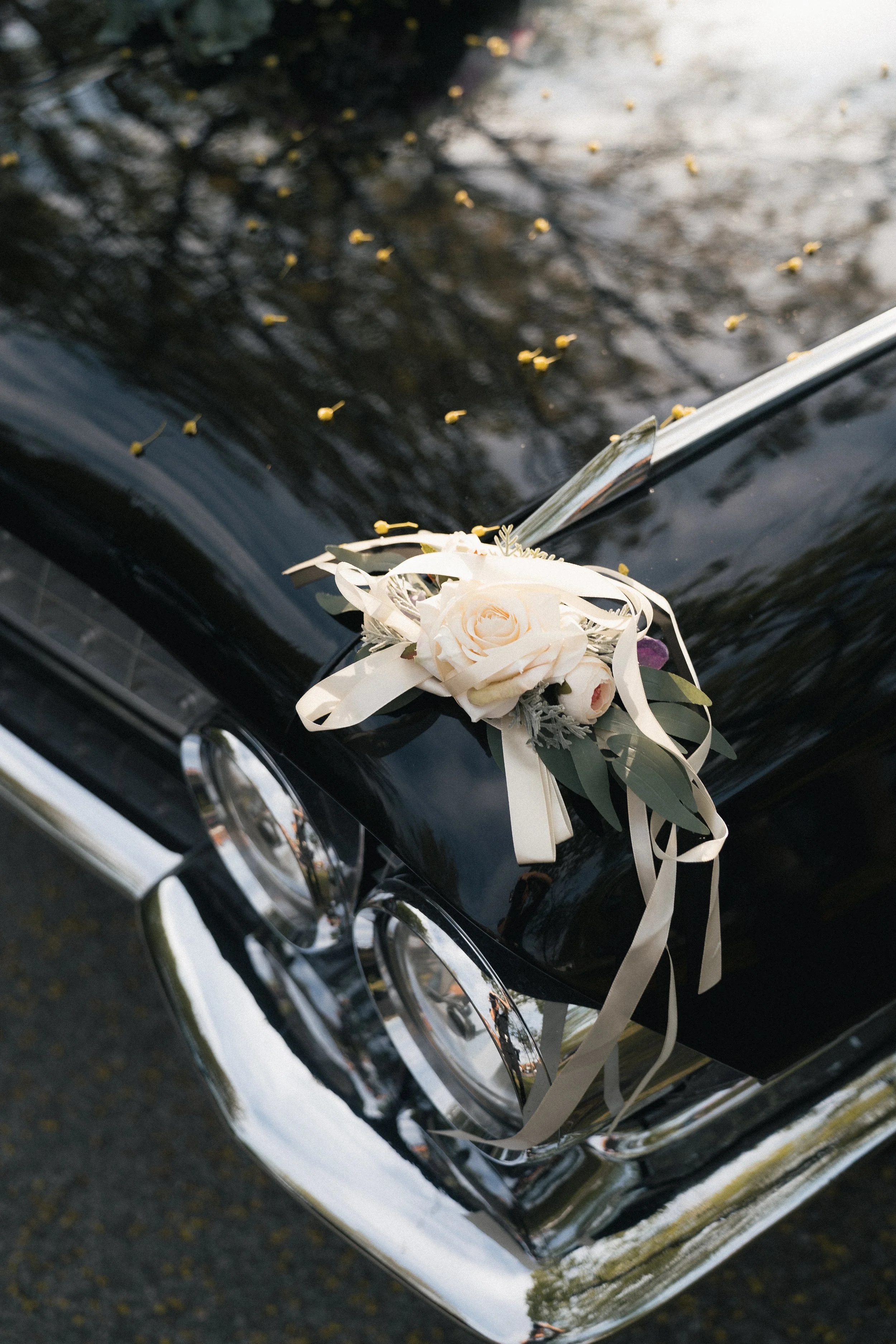 Ein schwarzes Auto mit einem Blumenstrauß auf der Motorhaube, der in der Nähe eines Wasserpools steht, mit Reflexionen von Bäumen im Wasser.