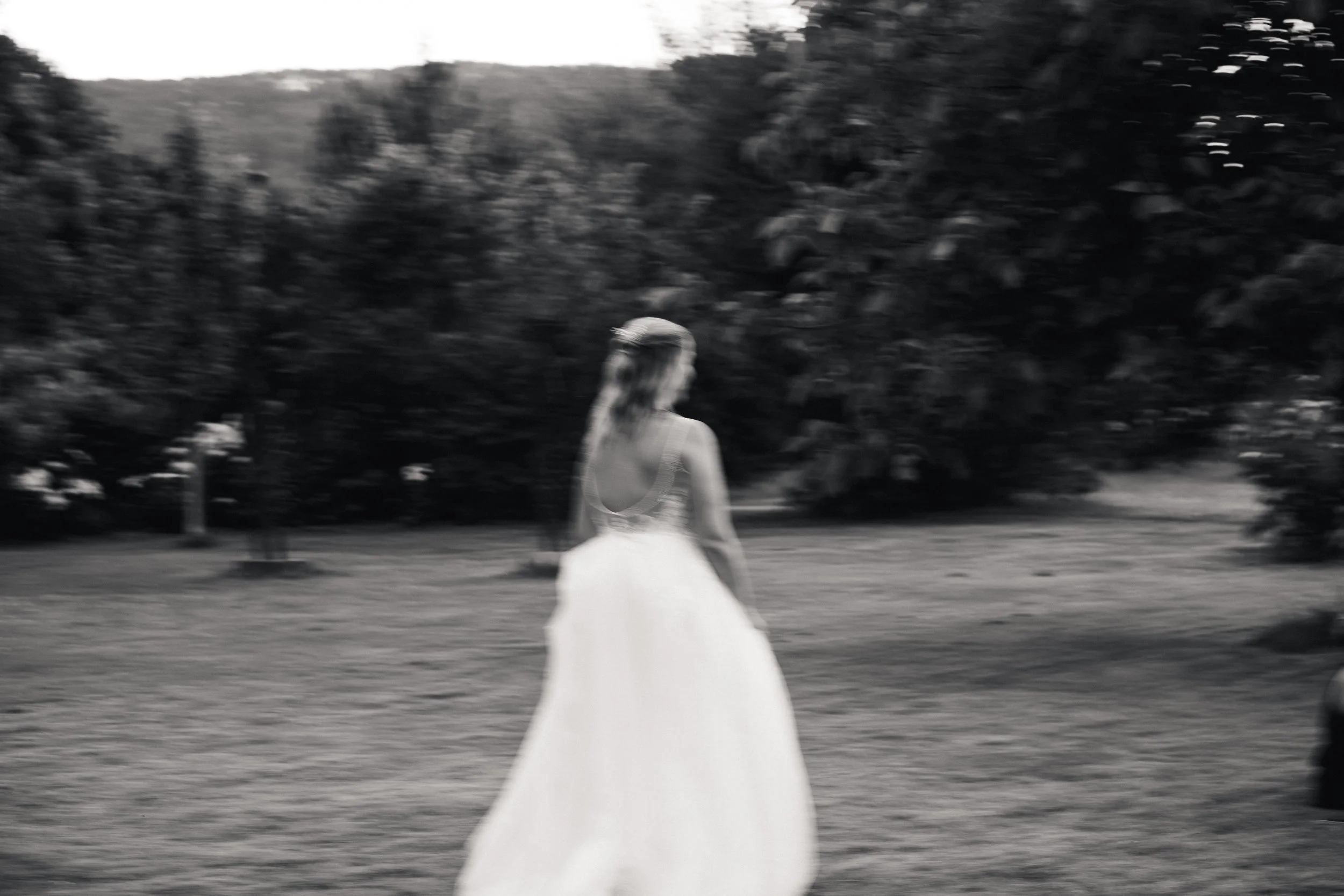 Schwarz-weiß-Foto eines Mädchens in einem weißen Kleid, das auf einer Wiese sitzt, mit Bäumen im Hintergrund.