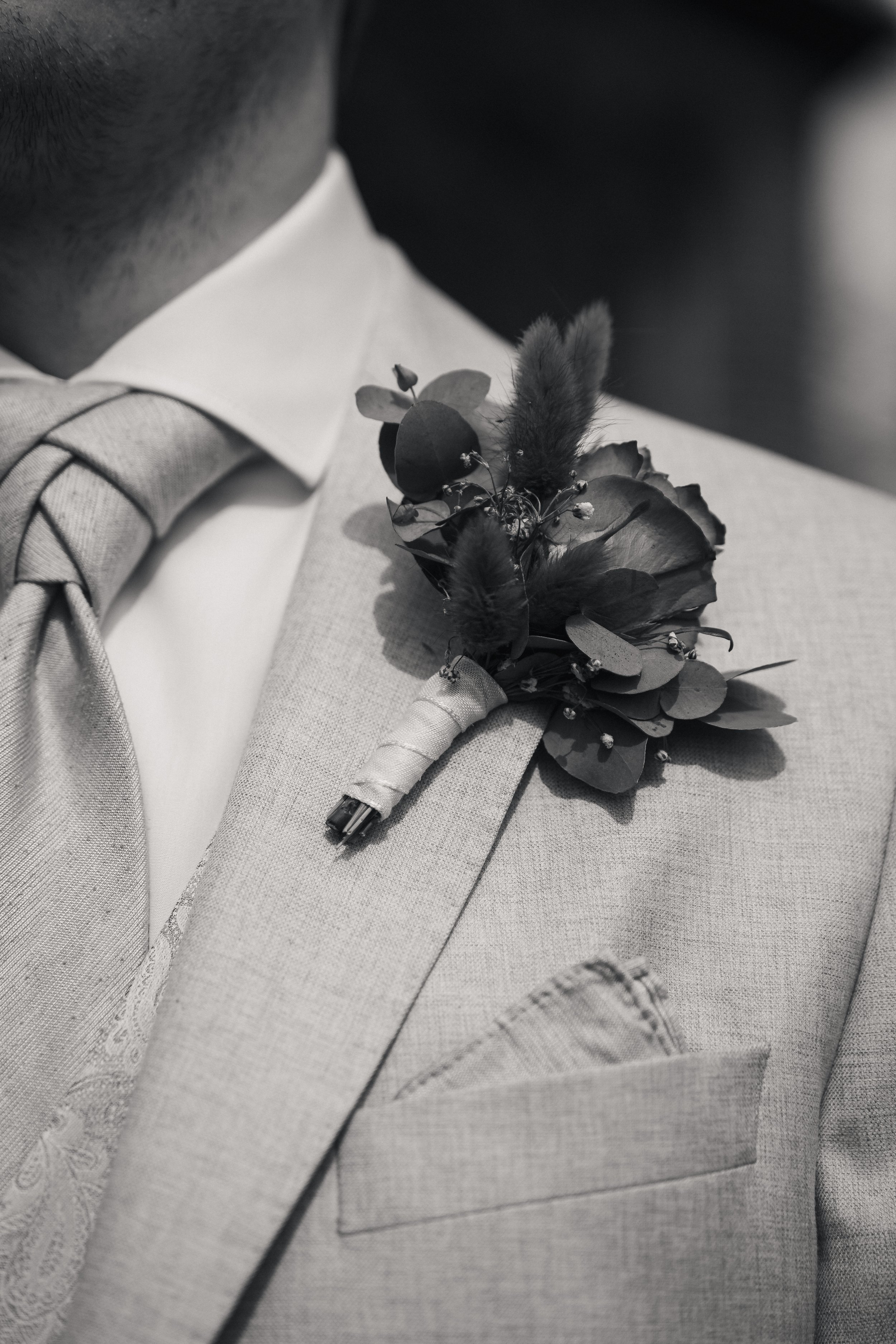 Nahaufnahme eines Anzugs oder Anzugjacke mit einem Blumen- und Federschmuck in Schwarz-Weiß.