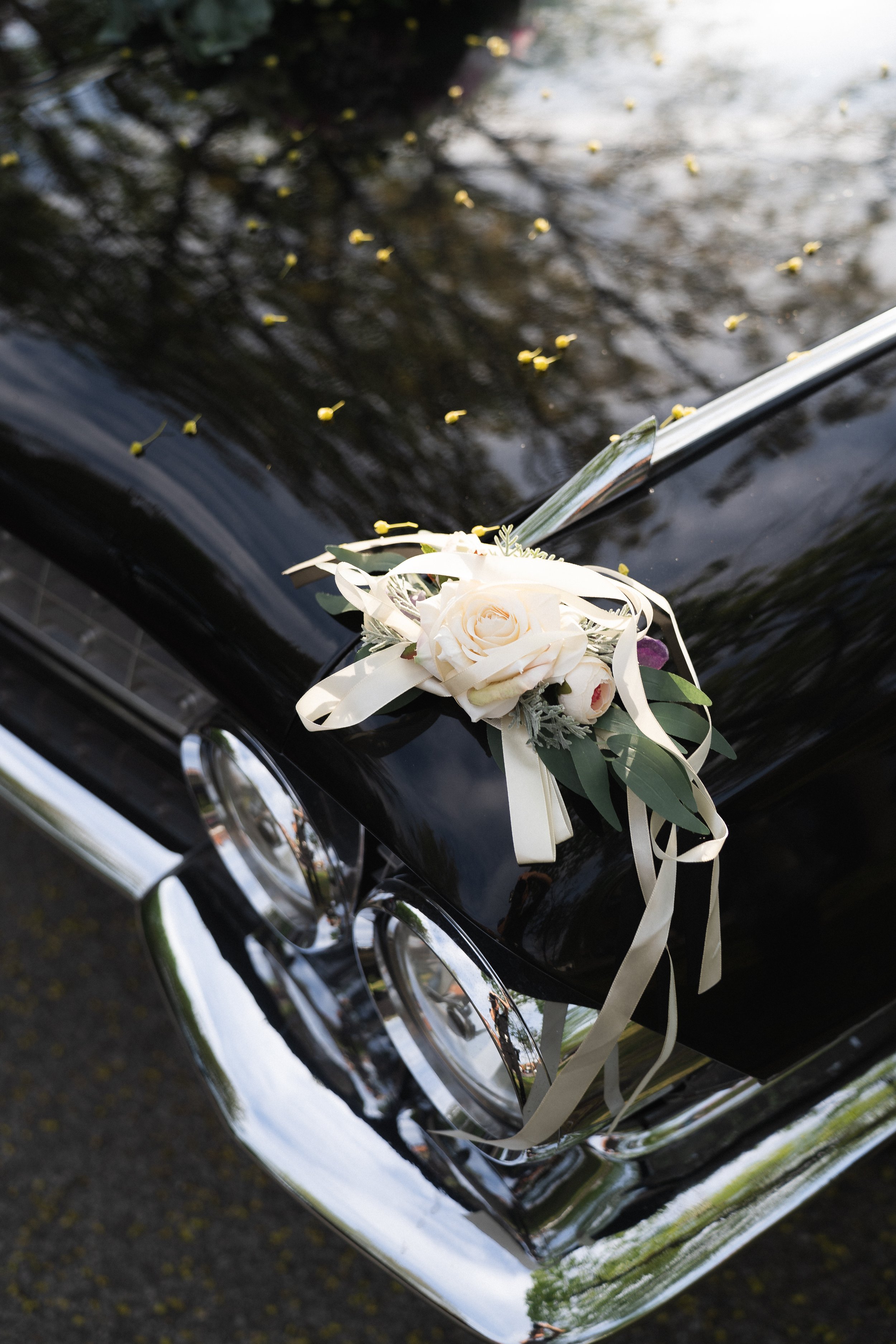 Ein schwarzer Luxuswagen mit Blumen- und Schleifenverzierung auf der Motorhaube, vermutlich für eine Hochzeit, fotografiert im Freien.