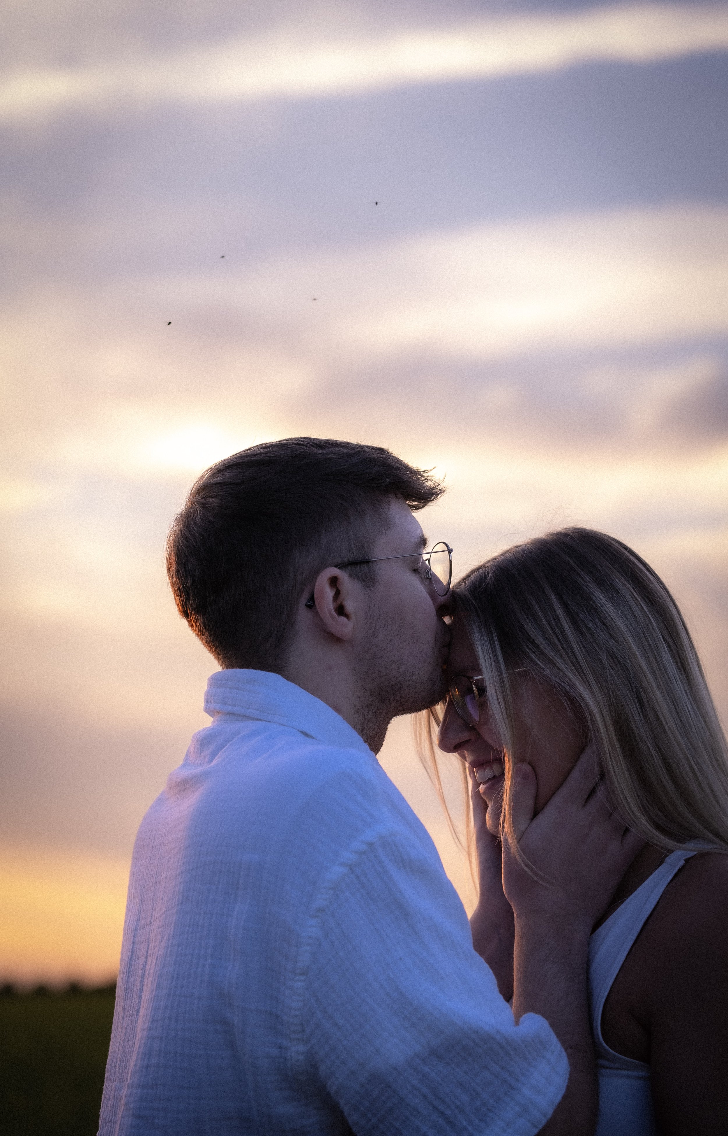 Ein verliebtes Paar beim Sonnenuntergang, der Mann küsst die Frau auf die Stirn.
