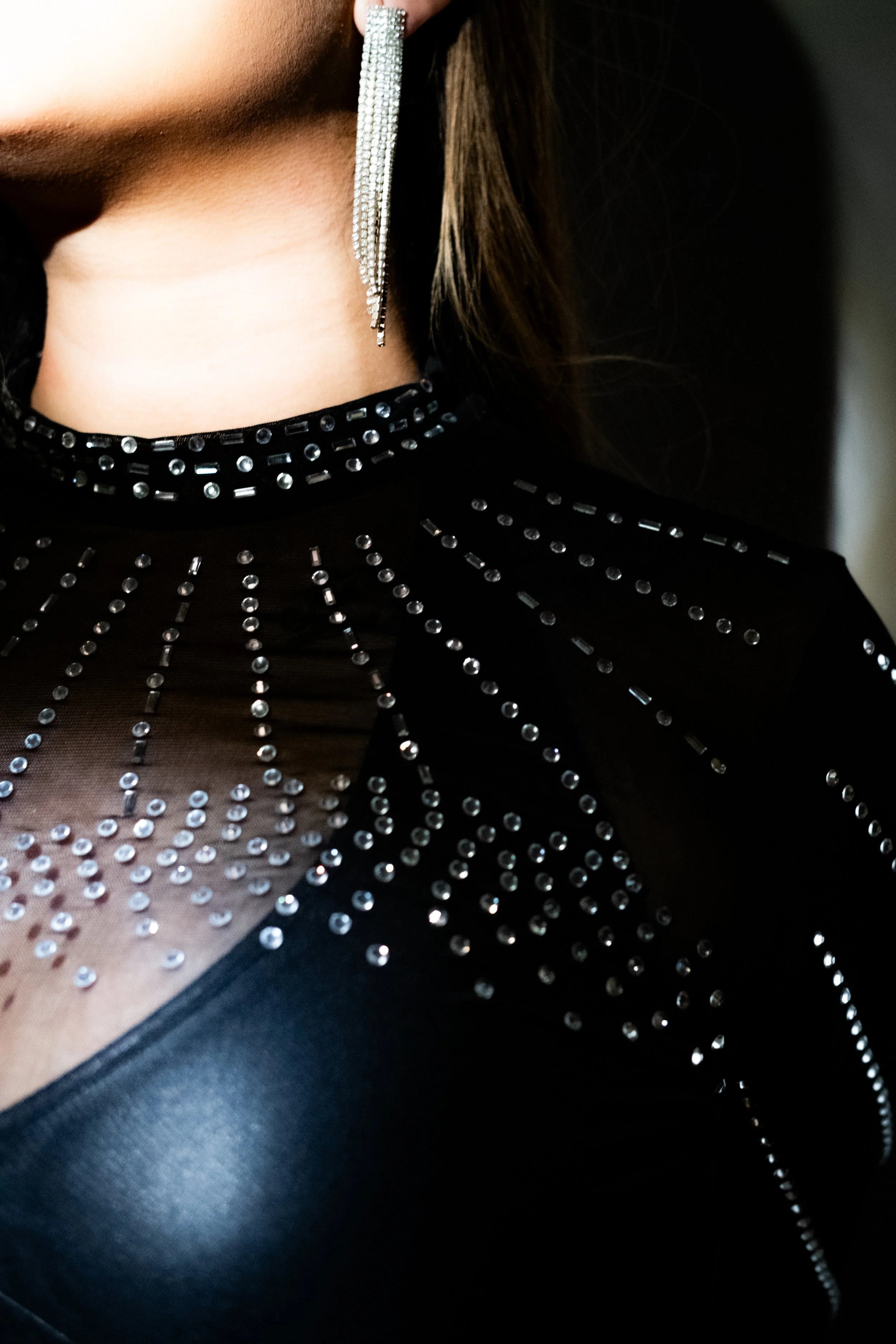 Nahaufnahme eines Damen-Kleids mit silbernen Nieten und Perlenverzierungen, dazu ein silbernes Kettenohrring.