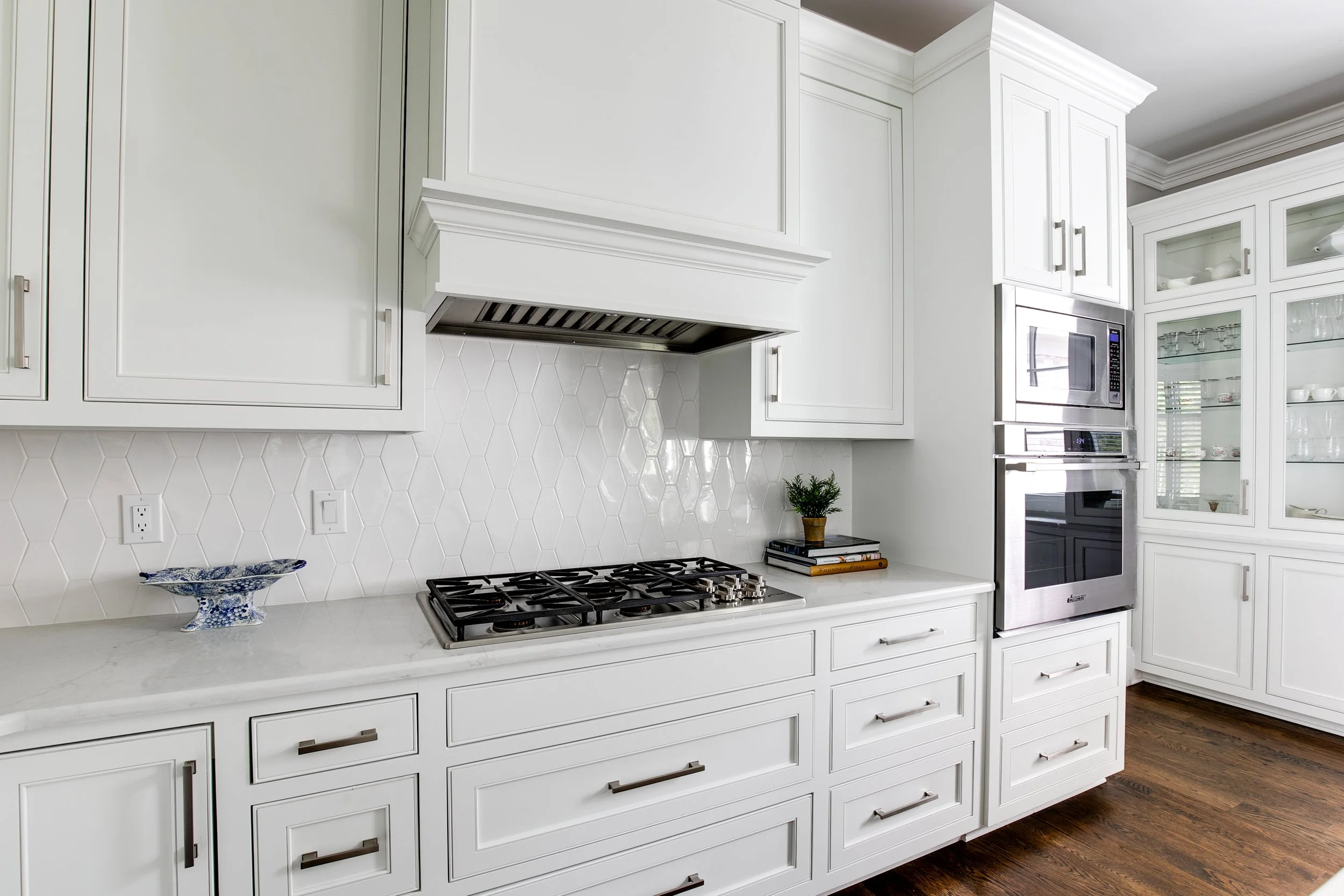 White kitchen with cabinets, a gas stove, built-in microwave and oven, a glass-front cabinet, and hardwood flooring.