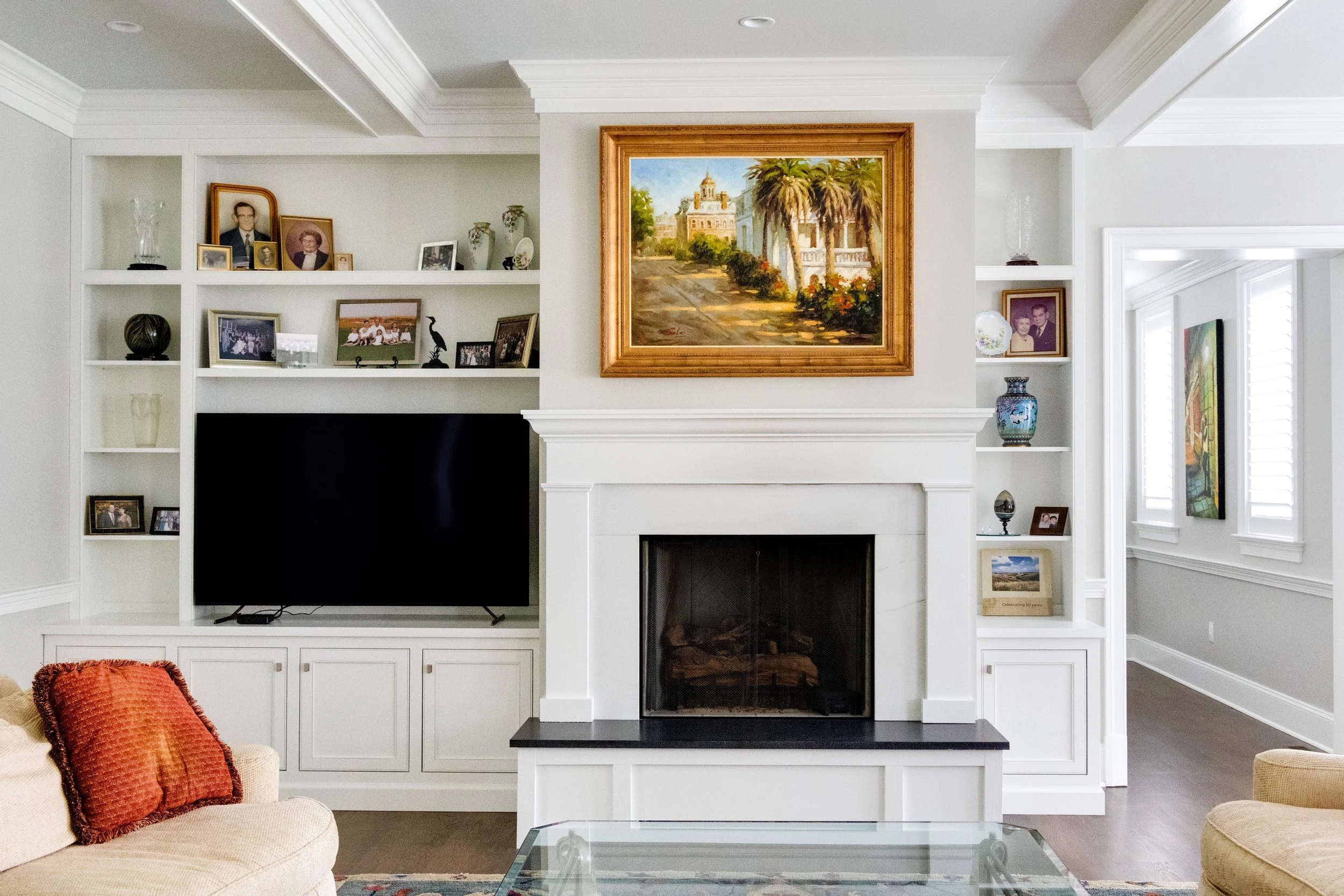 Living room with white built-in shelves, a white fireplace, a large framed painting above the fireplace, and a mounted flat-screen TV.