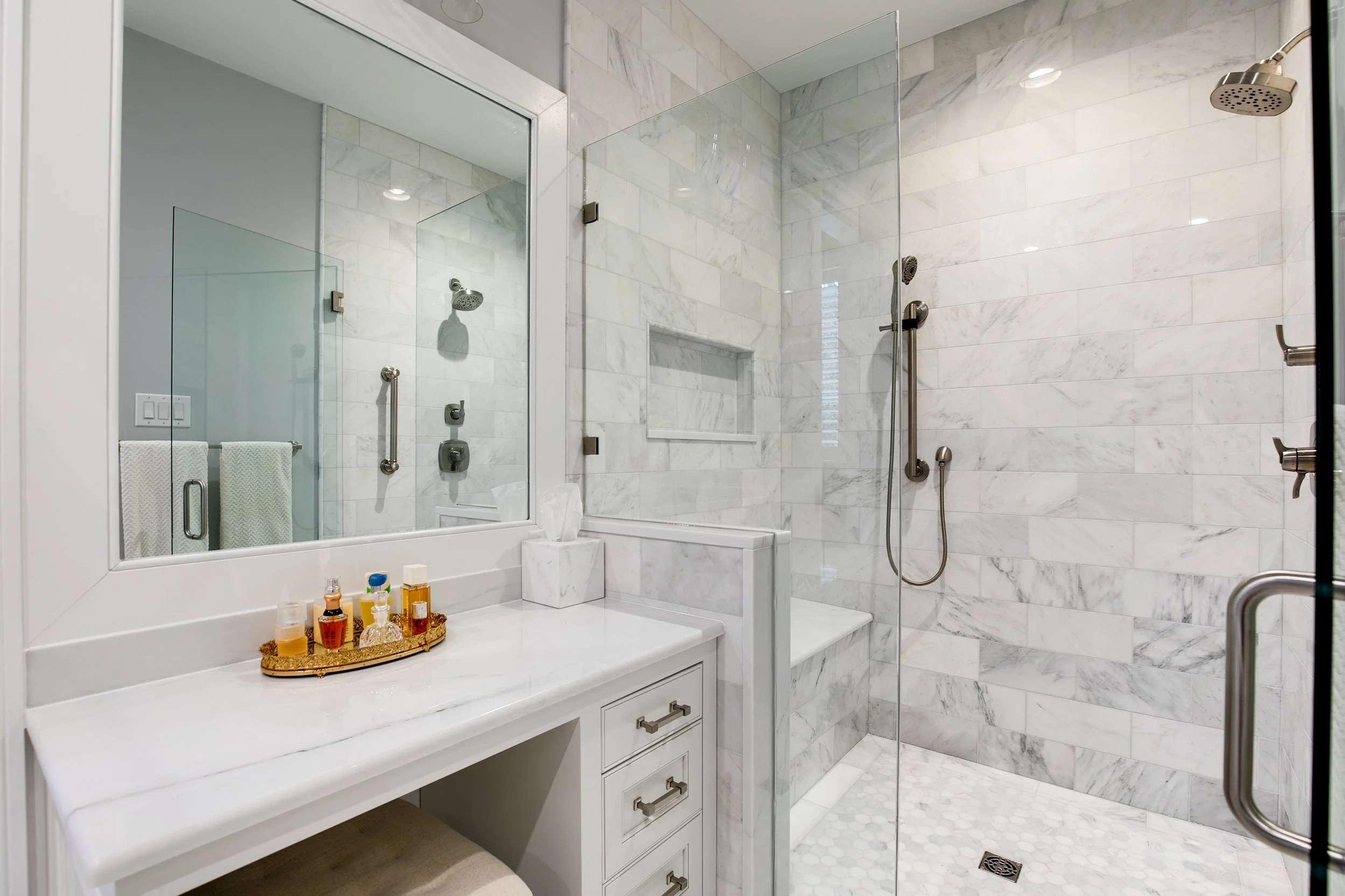 Modern marble bathroom with a glass-enclosed shower, white vanity with drawer storage, and a mirror reflecting the shower area.