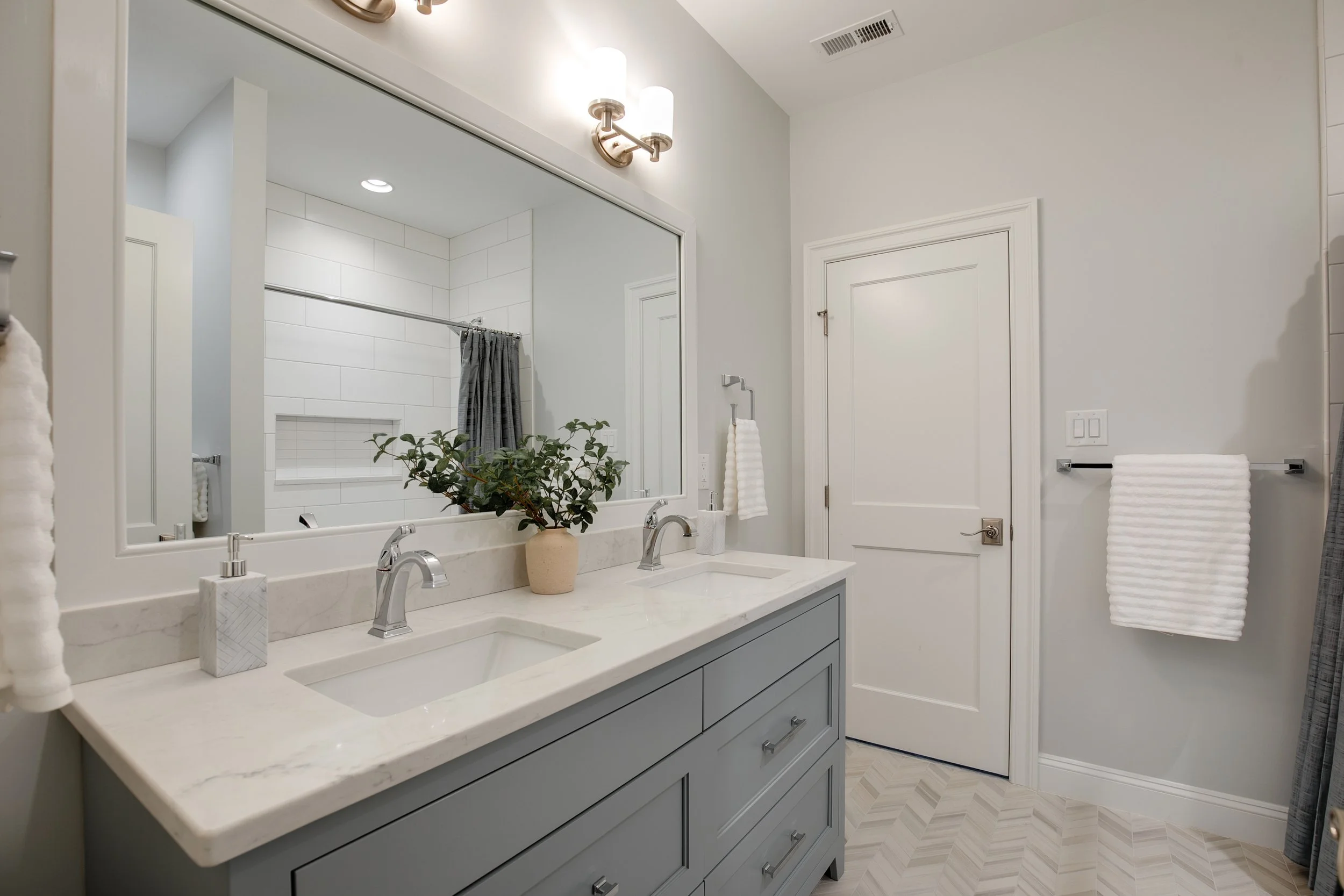 Modern bathroom with double sink vanity, large mirror, potted plant, towel holder, white towels, and shower area with gray curtain