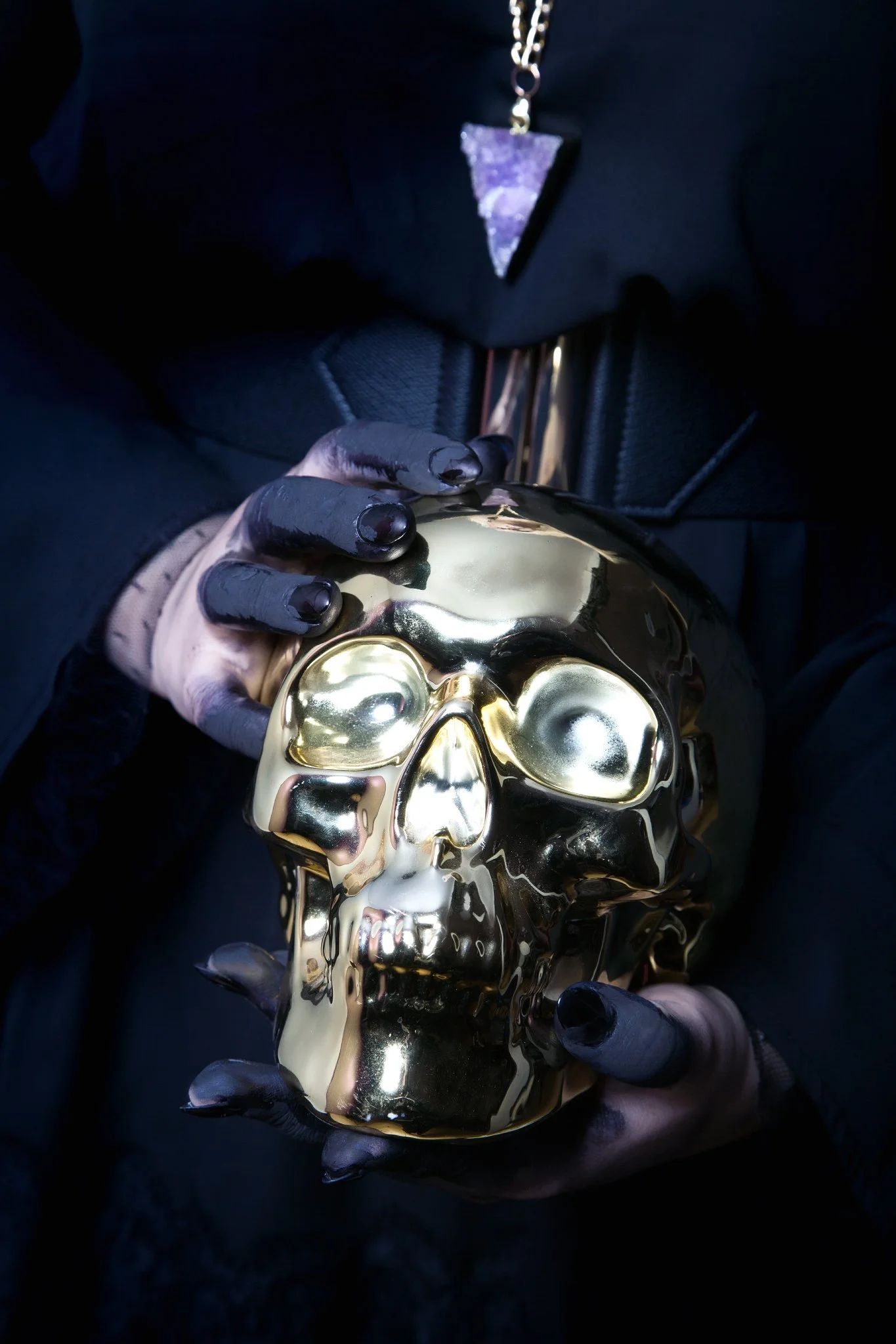 Person wearing black gloves holding a shiny, gold-colored skull sculpture.
