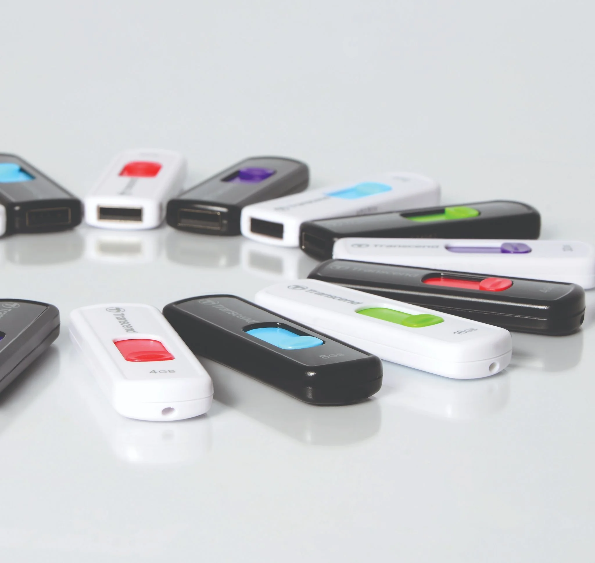 Collection of USB modems in various colors, including white, black, and gray, with colored sliding buttons, arranged on a reflective white surface.