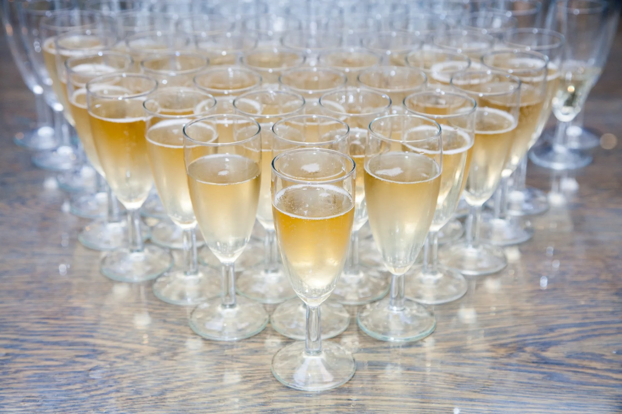 Multiple glasses of champagne arranged on a wooden table.