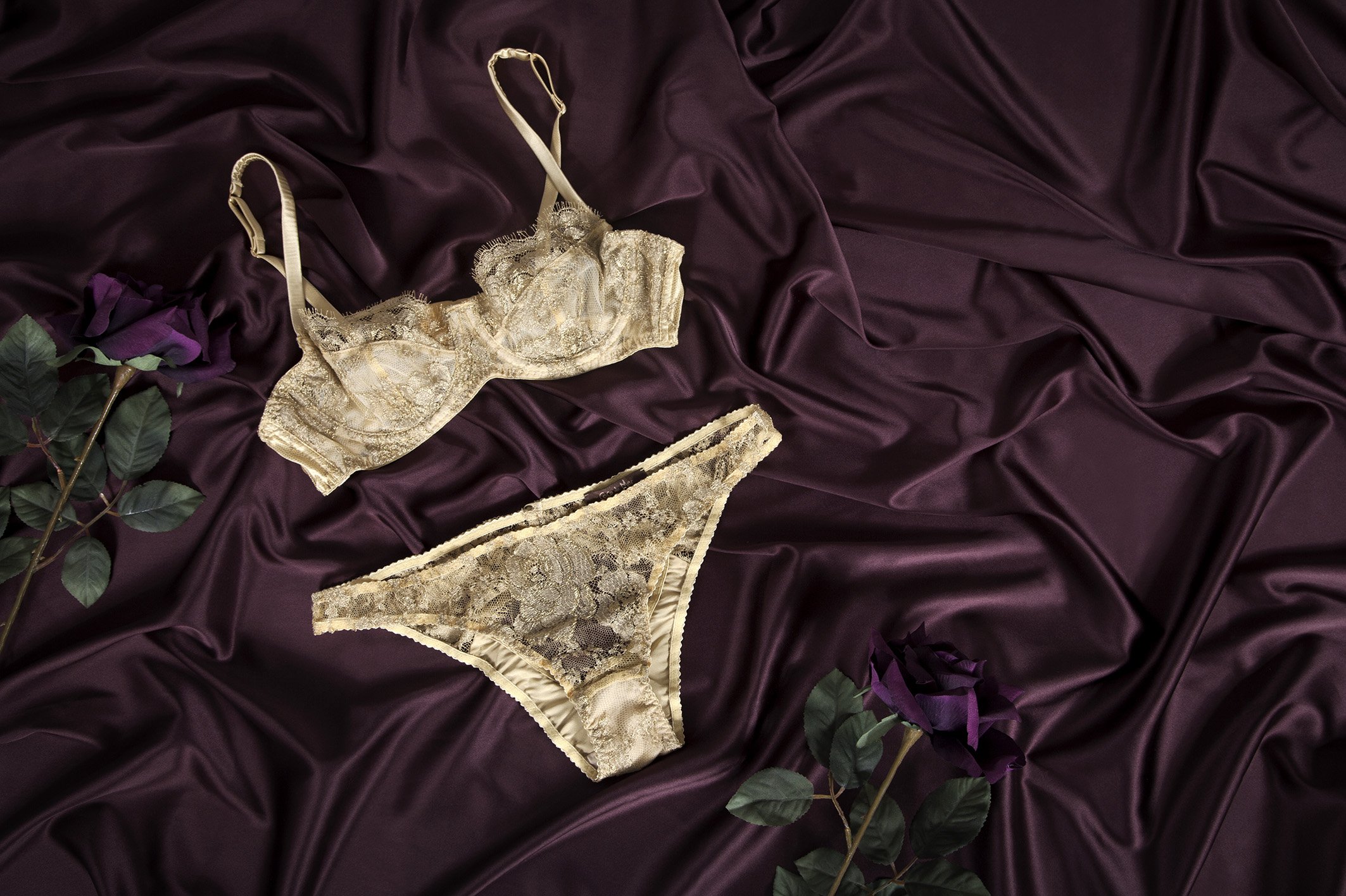 Lingerie set including a beige lace bra and matching panties on purple silky fabric with purple roses.
