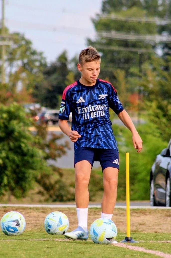 Boy in soccer uniform practicing dribbling around soccer balls on a field.