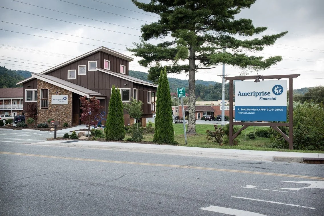 A commercial building with signs for Ameriprise Financial, featuring a large sign on the lawn, trees, and a street in the foreground.