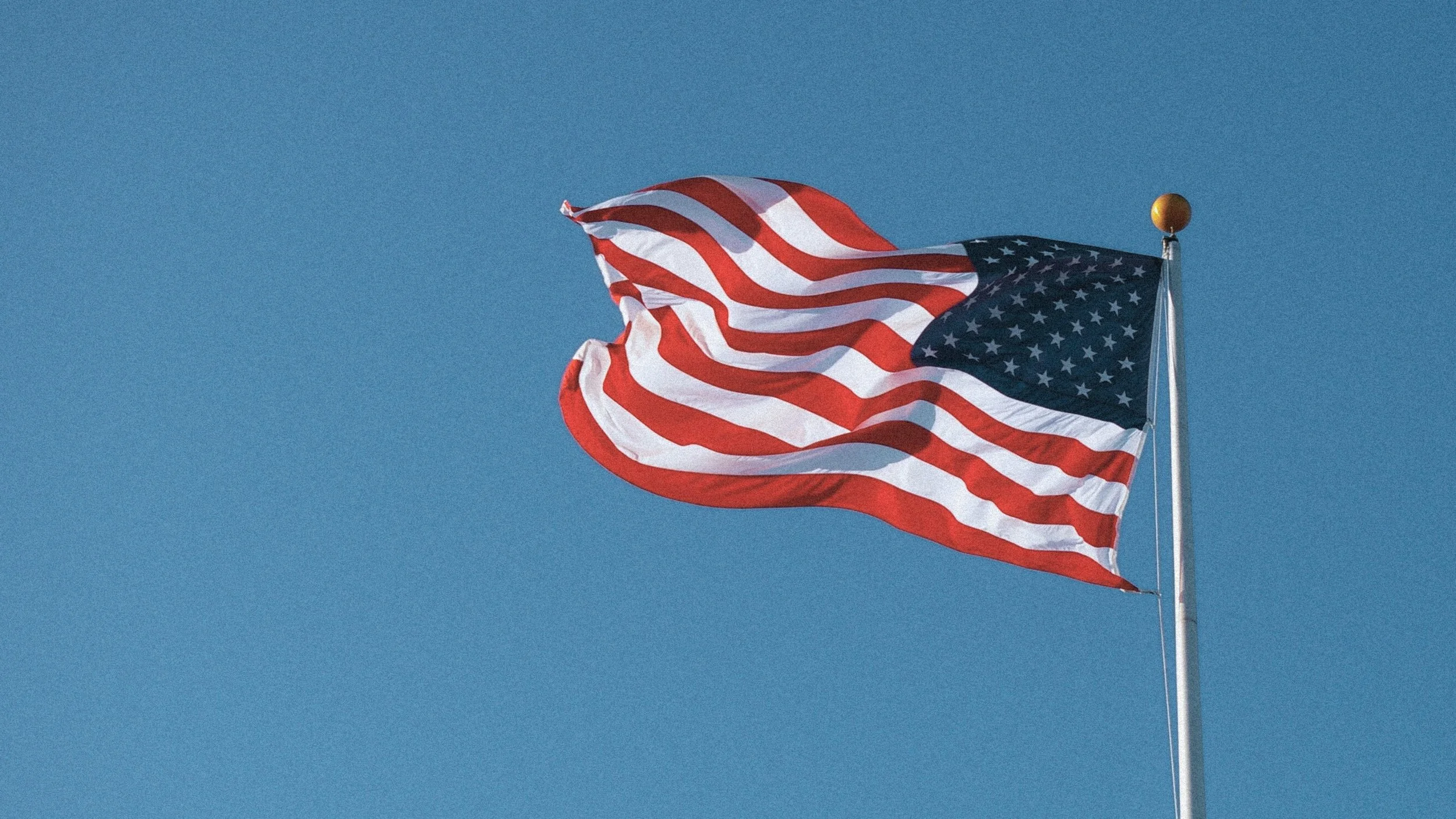 American flag waving on a clear blue sky.