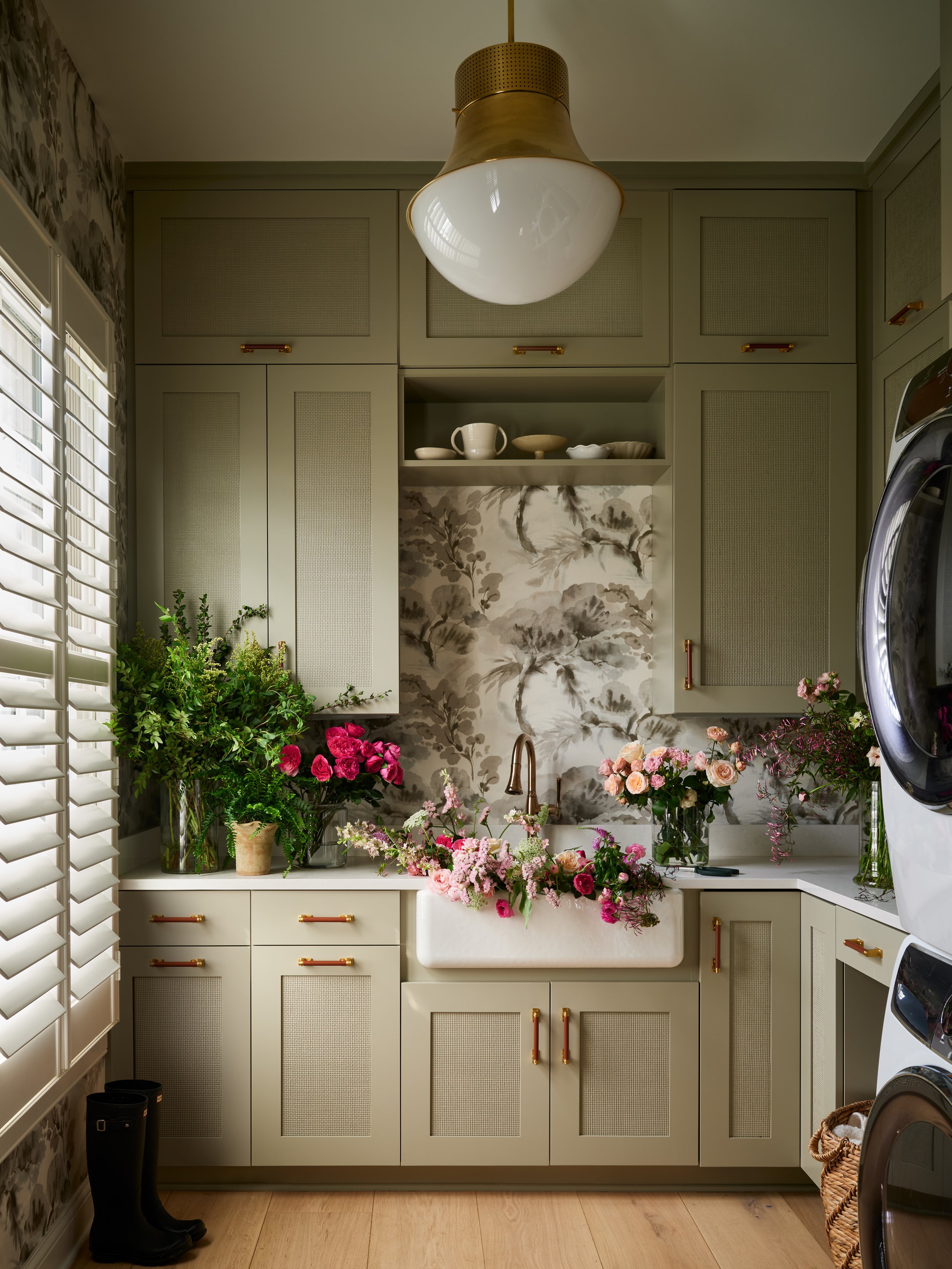 Kitchen with green cabinets, floral wallpaper, a white farmhouse sink, and multiple bouquets of pink and white flowers on the counter.