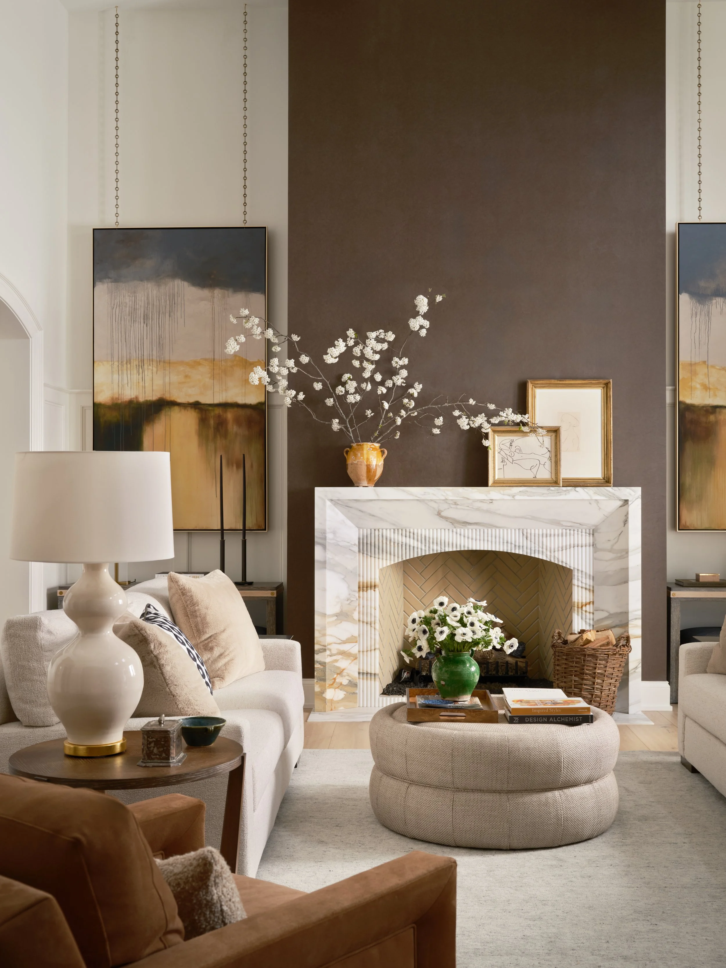 Living room with a marble fireplace, floral arrangement, abstract paintings, and cozy furniture.
