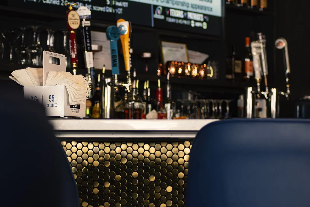 View of a bar counter with taps for draft beer, glasses, and a menu board in the background.