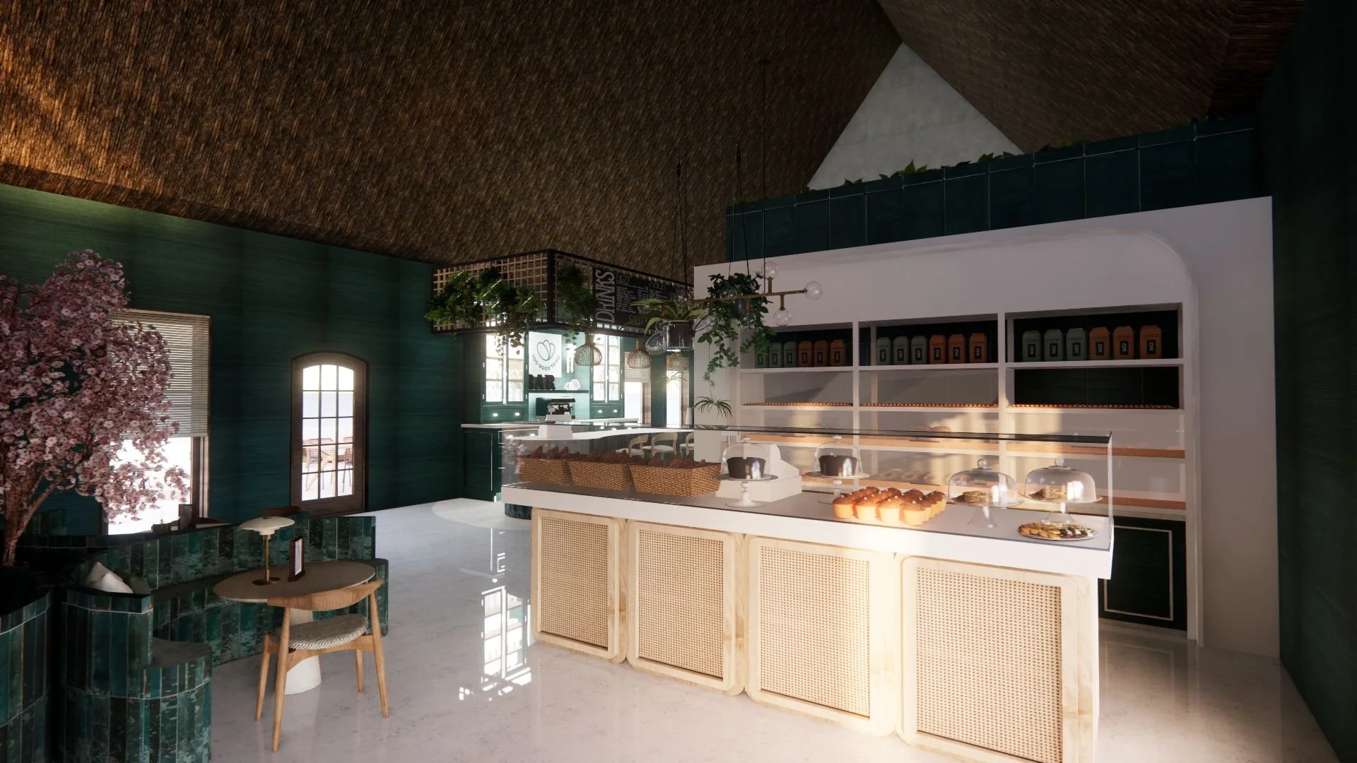Interior of a modern cafe with a white counter displaying baked goods under glass covers, dark green walls, a cherry blossom tree, and seating area with a round table and chairs.
