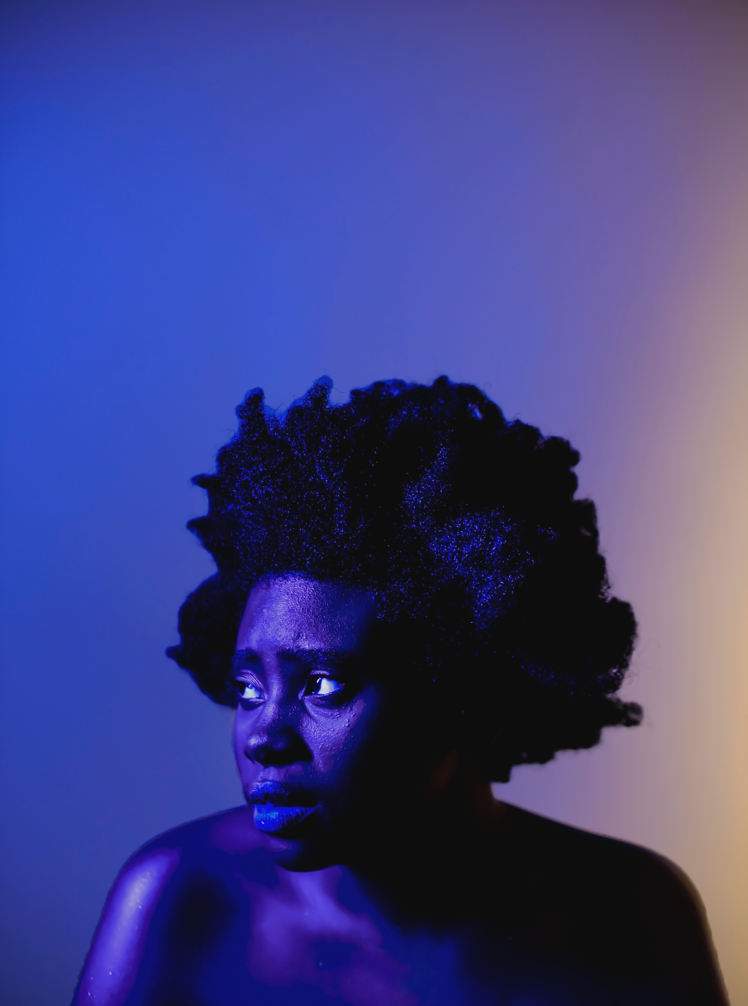 Portrait of a Black woman with natural hair looking to the side, illuminated with purple and blue lighting.
