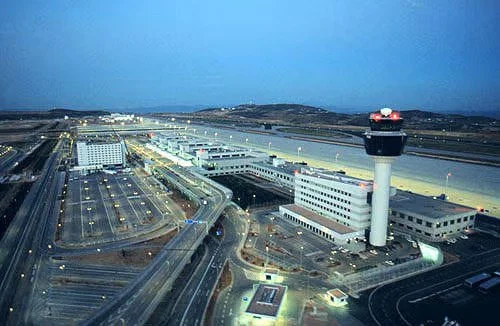 Overview of an airport with runways, terminal buildings, and an air traffic control tower at dusk.