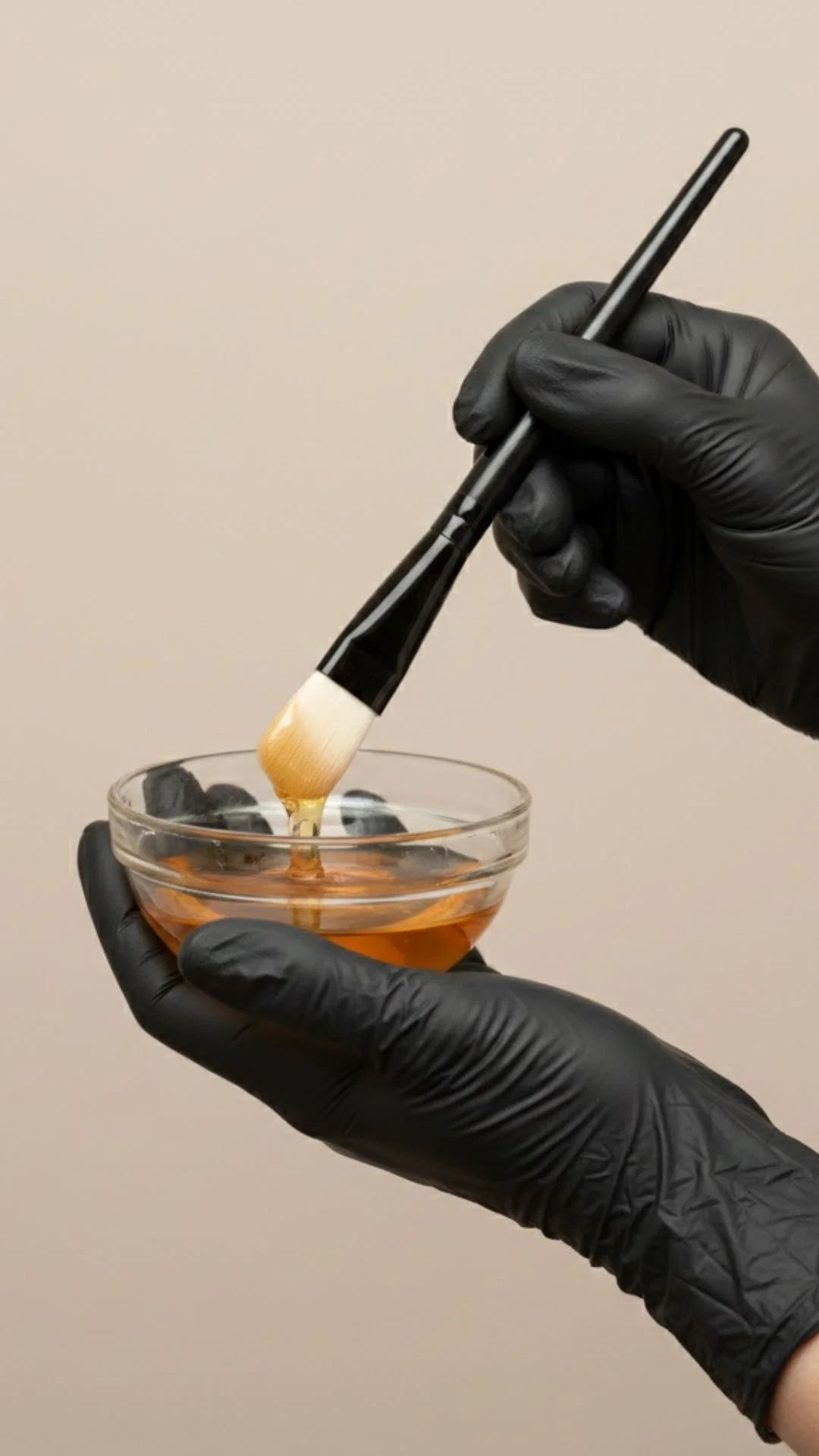 Black gloved hands holding a clear glass bowl of chemical peel materials
