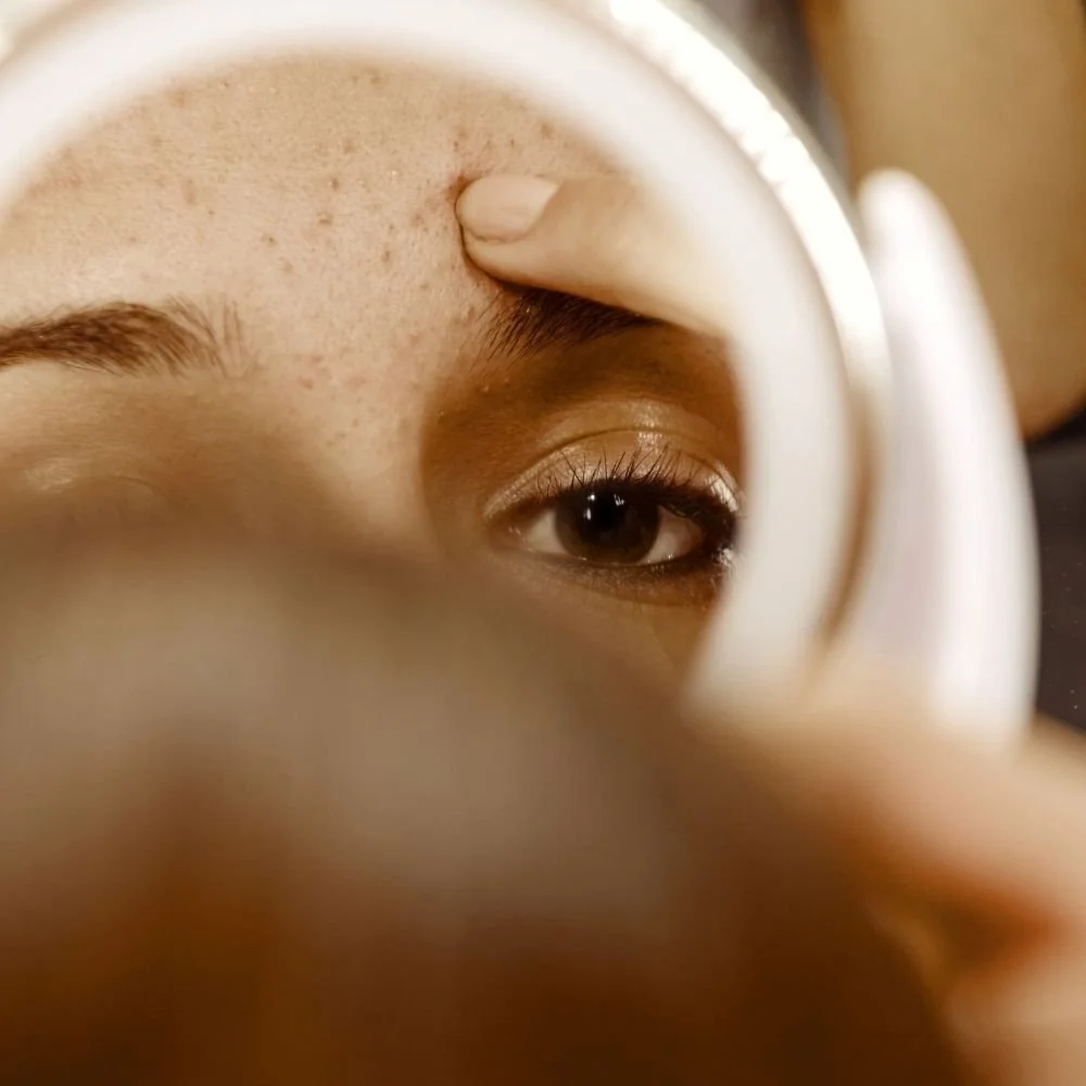 Woman looking in the mirror and noticing a skin imperfection