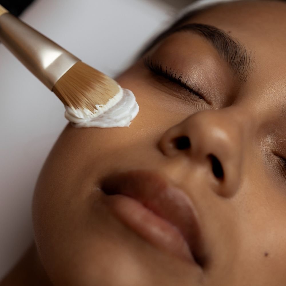 Chemical peel product being applied to a female client's cheek with a brush