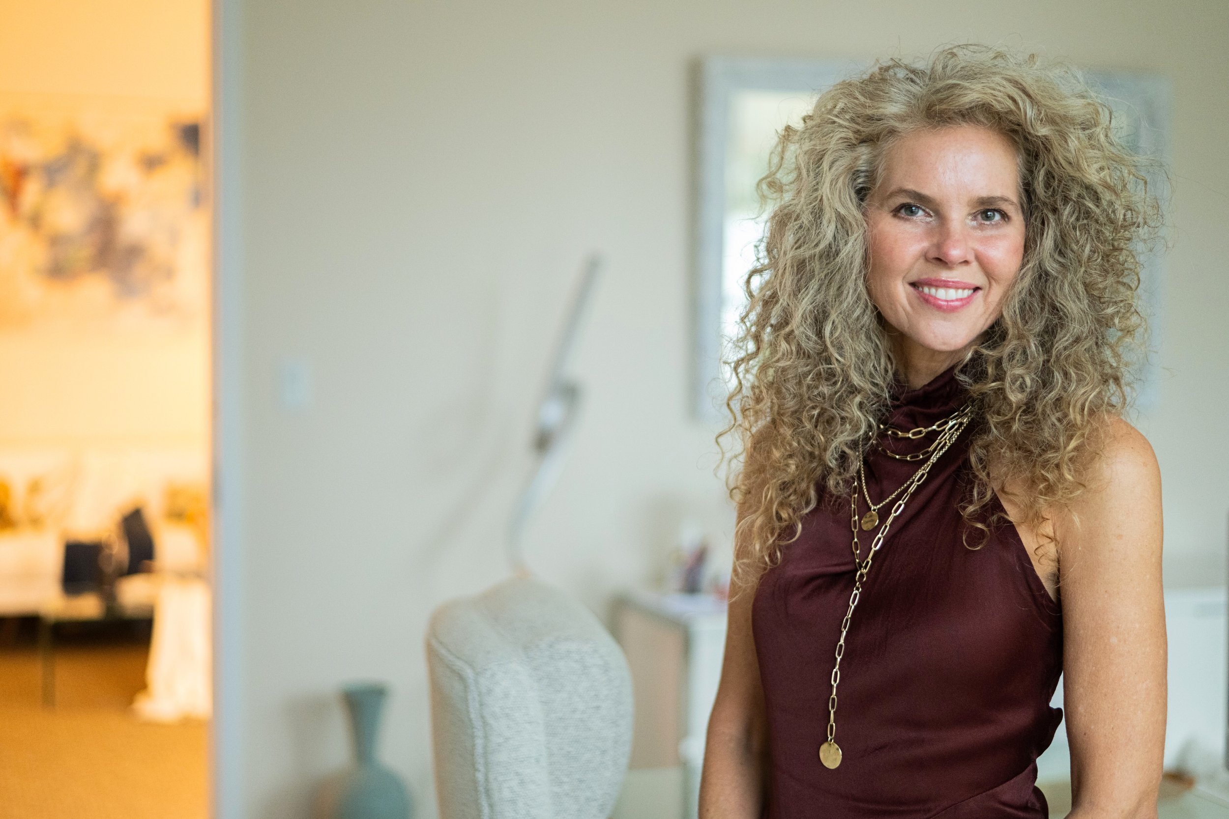 A woman with curly blonde hair smiling in a well-lit room.