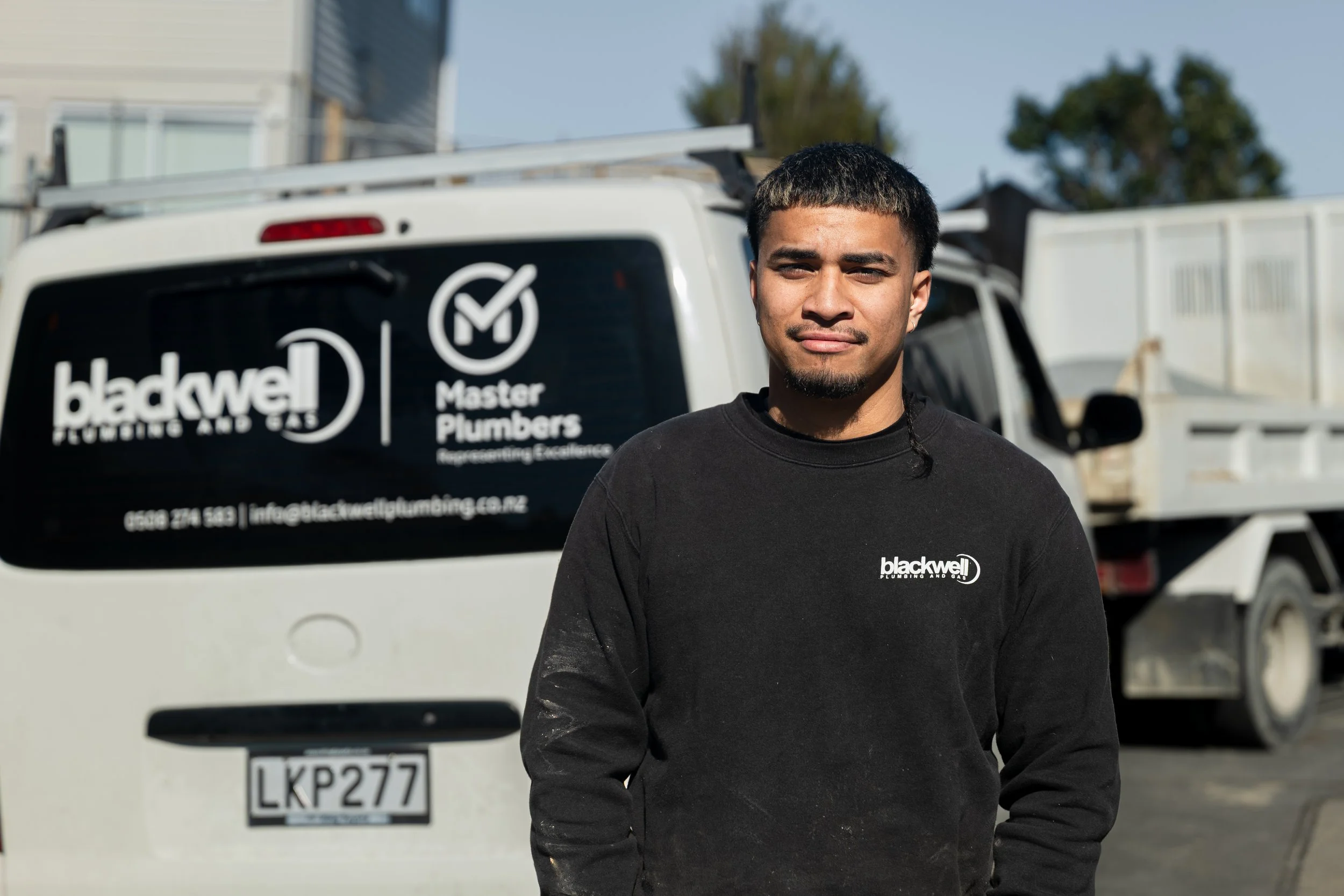 A man standing outdoors in front of a white service van with Blackwell Plumbing and Gas logos.