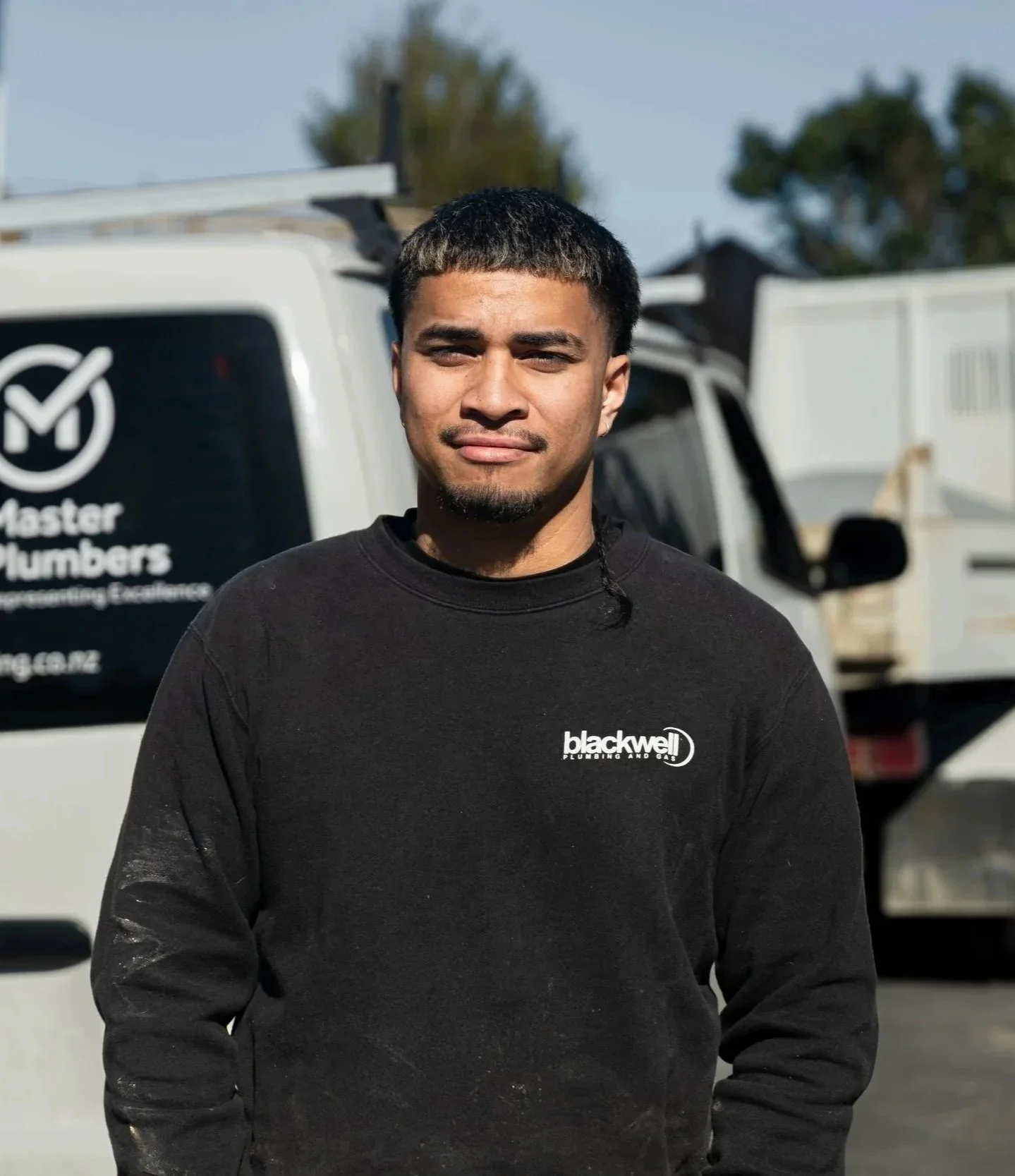 A man standing outdoors in front of a white service van with Blackwell Plumbing and Gas logos.