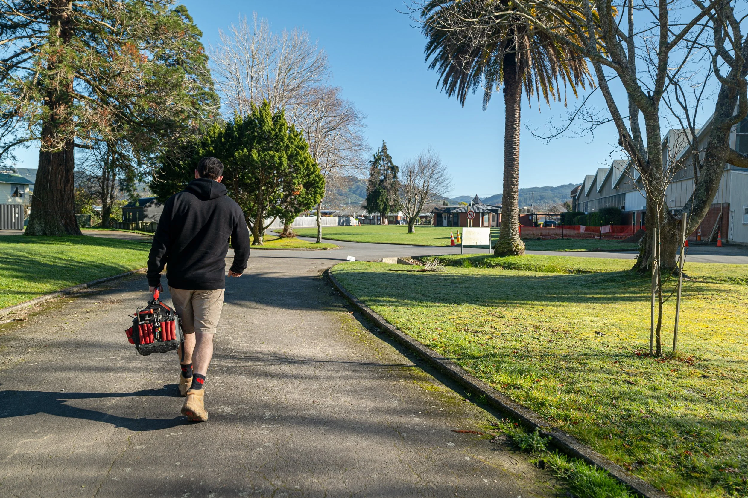 A Blackwell Plumbing and Gas employee walking down a path outdoors with a tool bag in hand.