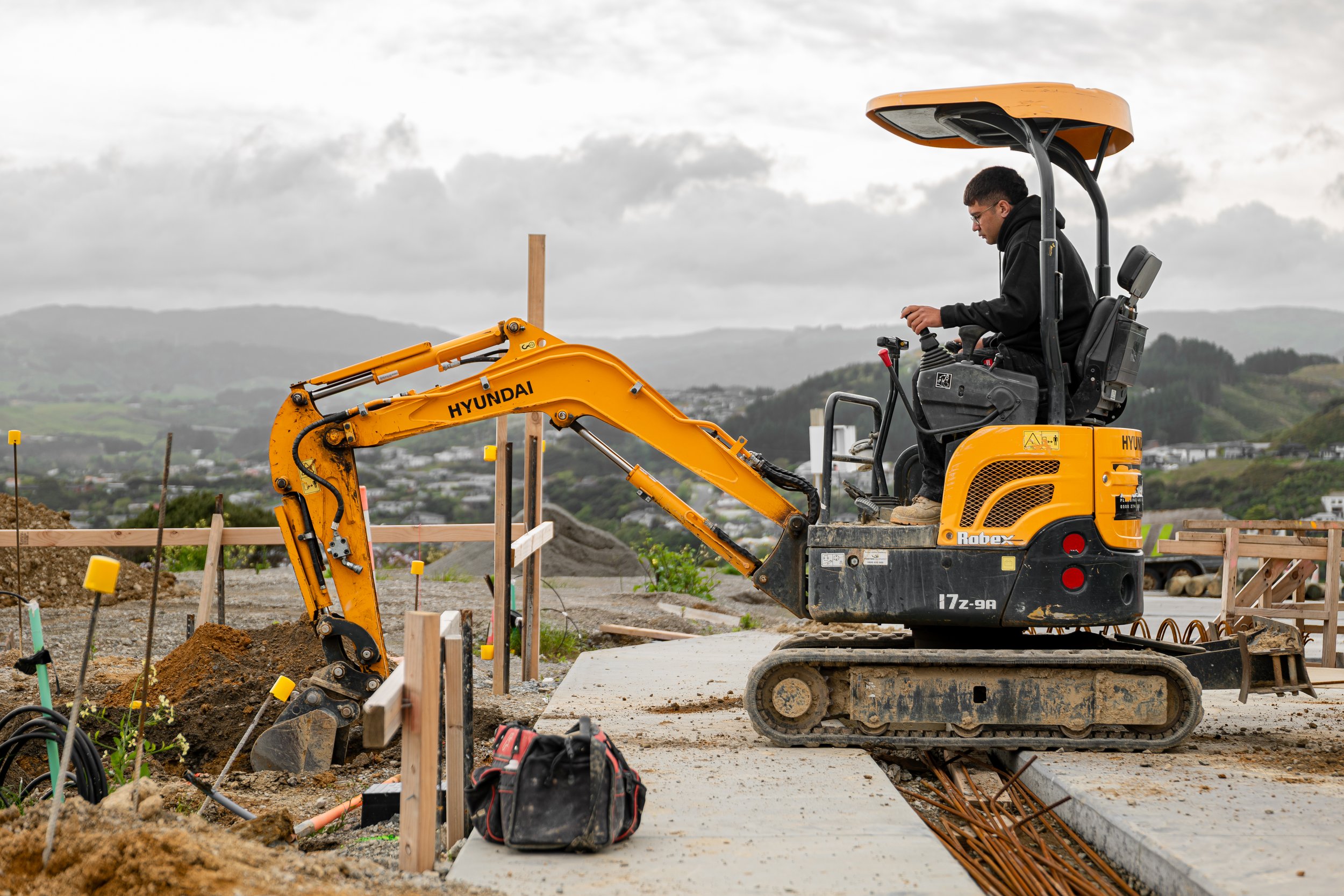 A yellow digger being driven by a Blackwell Plumbing and Gas employee outside.