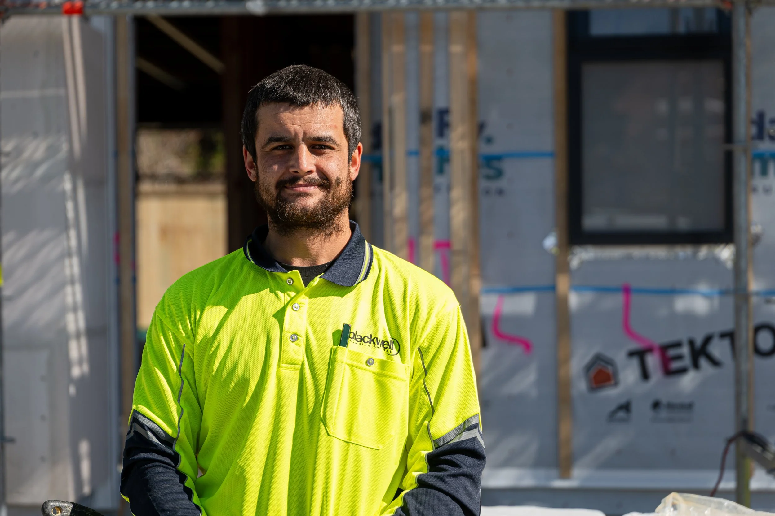 Construction worker in a bright yellow safety shirt standing in front of a building under construction.