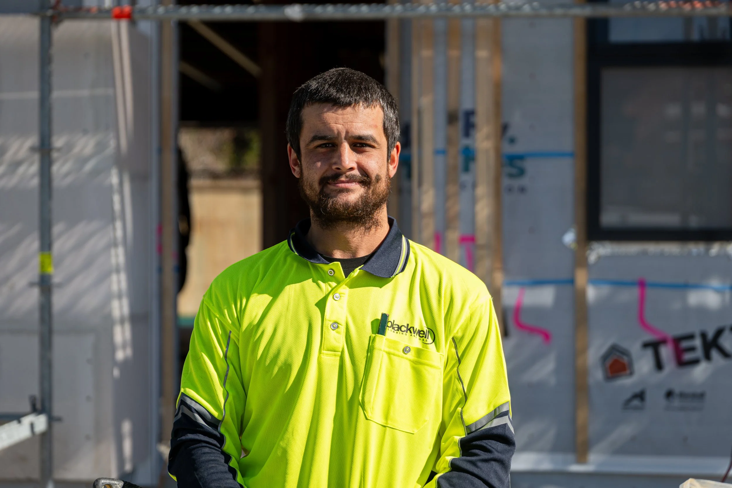 Construction worker in a bright yellow safety shirt standing in front of a building under construction.