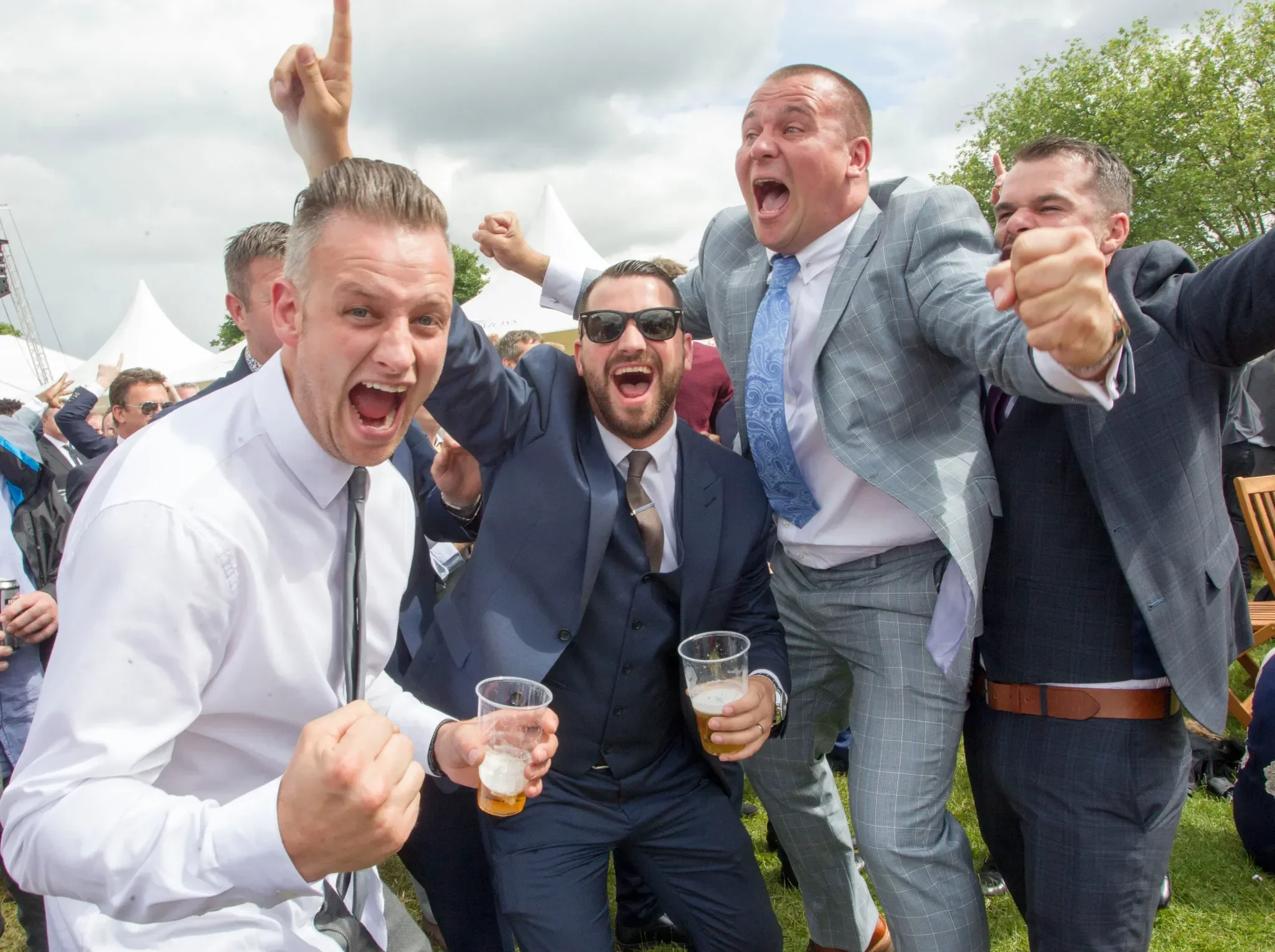 Group of men celebrating outdoors at a party or event, wearing suits and holding drinks, with cheerful expressions and energetic poses at an Osman Racing Club member's day.