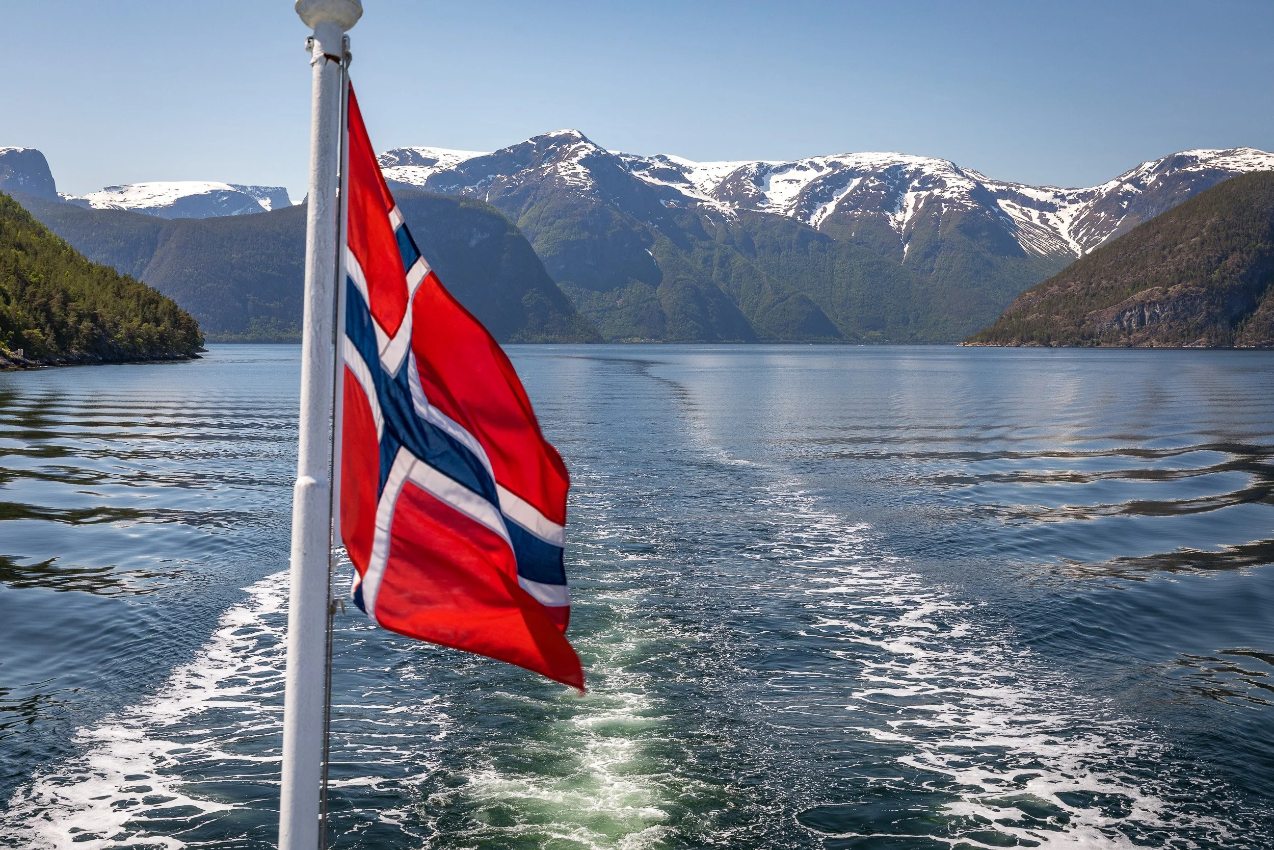 A quiet shoreline in Hardangerfjorden — cabins and boathouses tucked into the greenery, surrounded by vast fjord scenery.